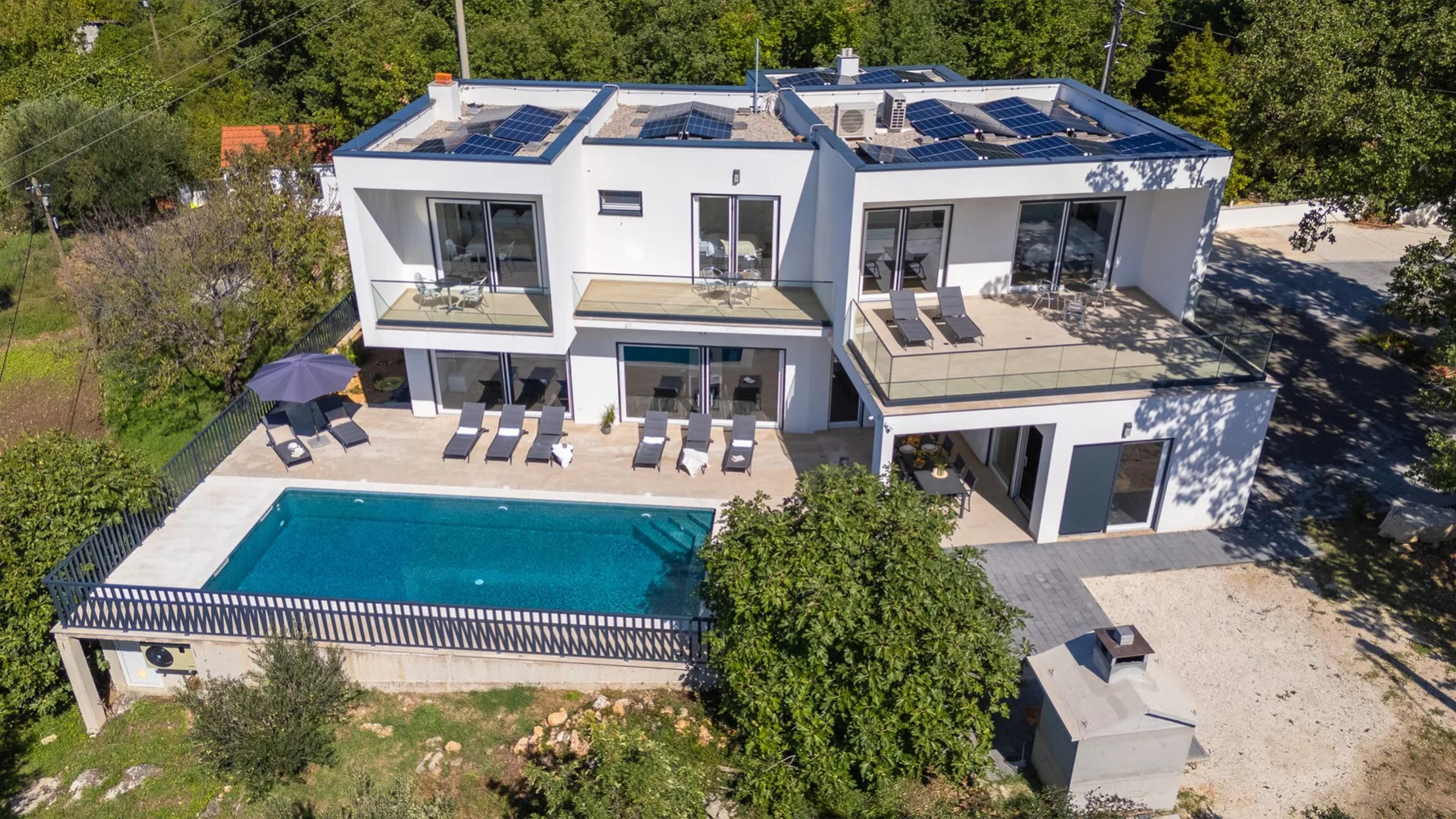 A modern white house overlooks a swimming pool and outdoor seating.