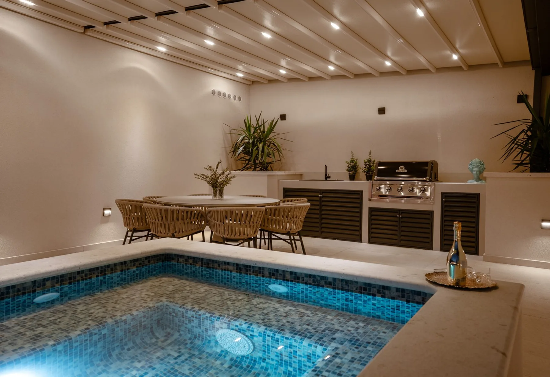 An indoor pool sits beside a counter with a built-in grill and seating.