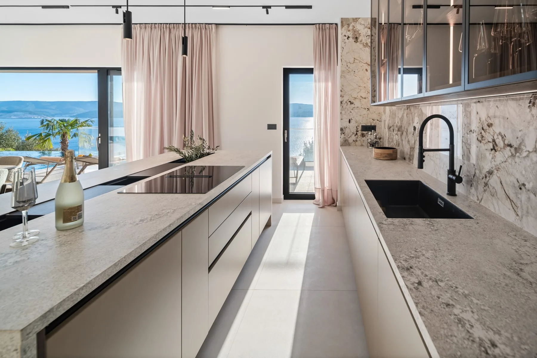 A bright modern kitchen with a long island and large windows overlooking the sea.