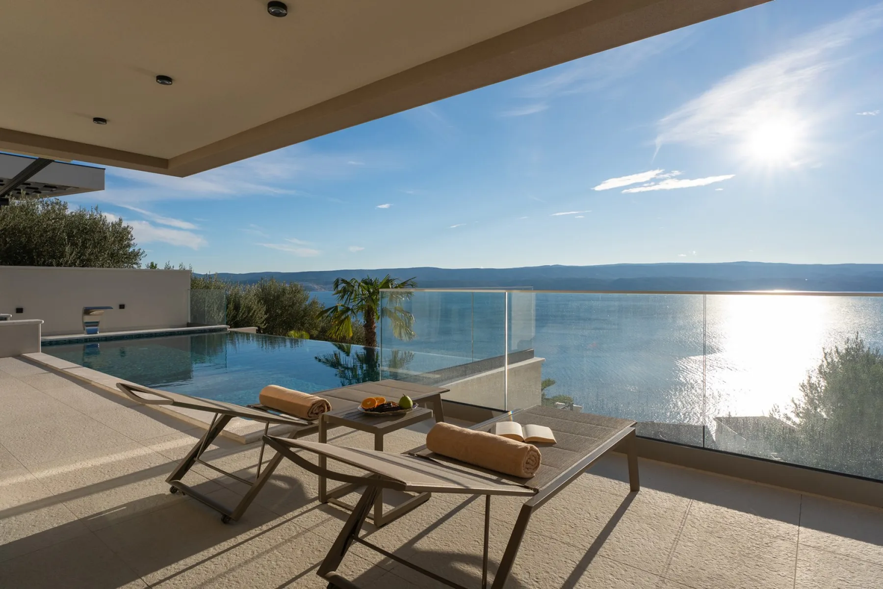 A poolside terrace overlooks the water, with lounge seating and a glass railing.