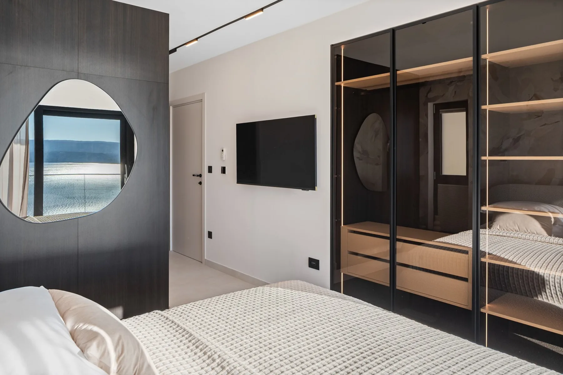 A modern bedroom with a bed, wall-mounted television, and dark built-in cabinetry.