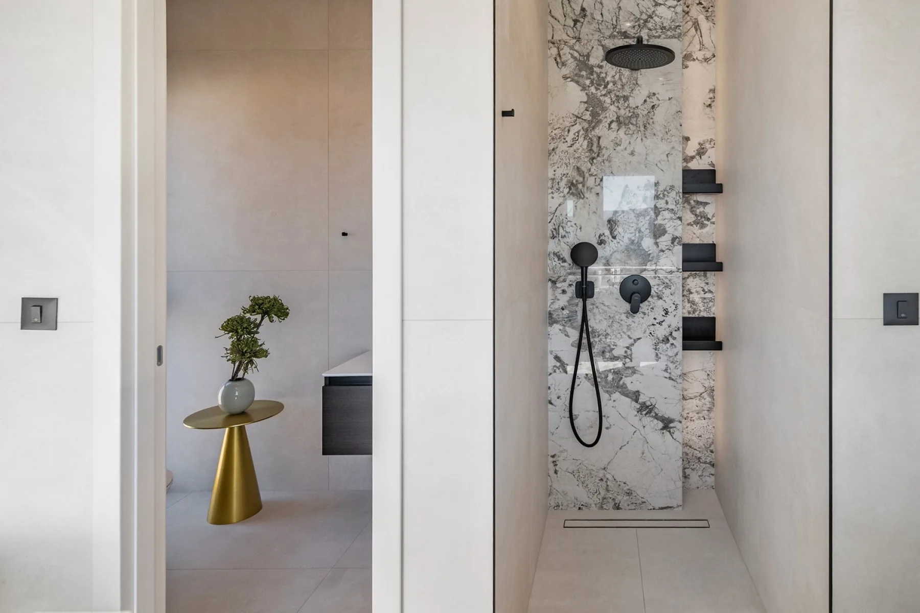 A modern bathroom with a walk-in shower and a small side table holding a plant.