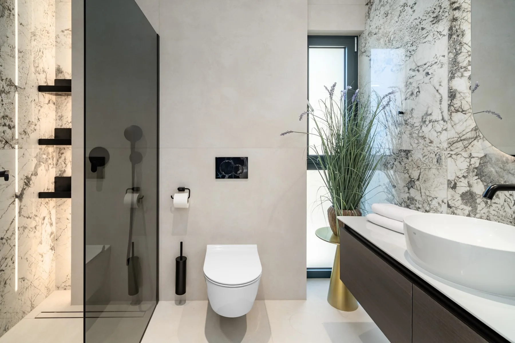 A modern bathroom with a wall-mounted toilet, glass shower, and a large sink.