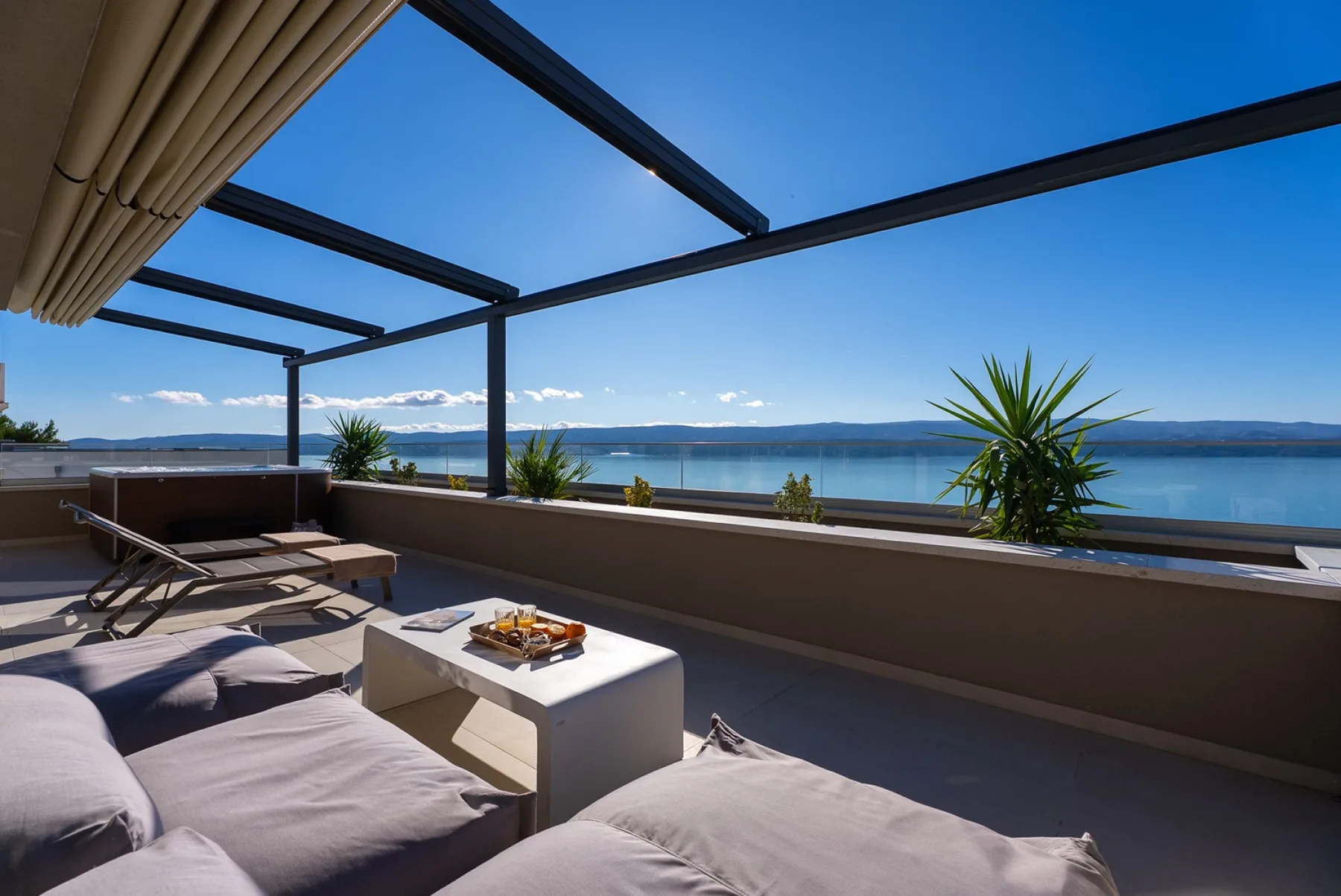 A terrace lounge overlooks the water, with cushioned seating beneath an open pergola.