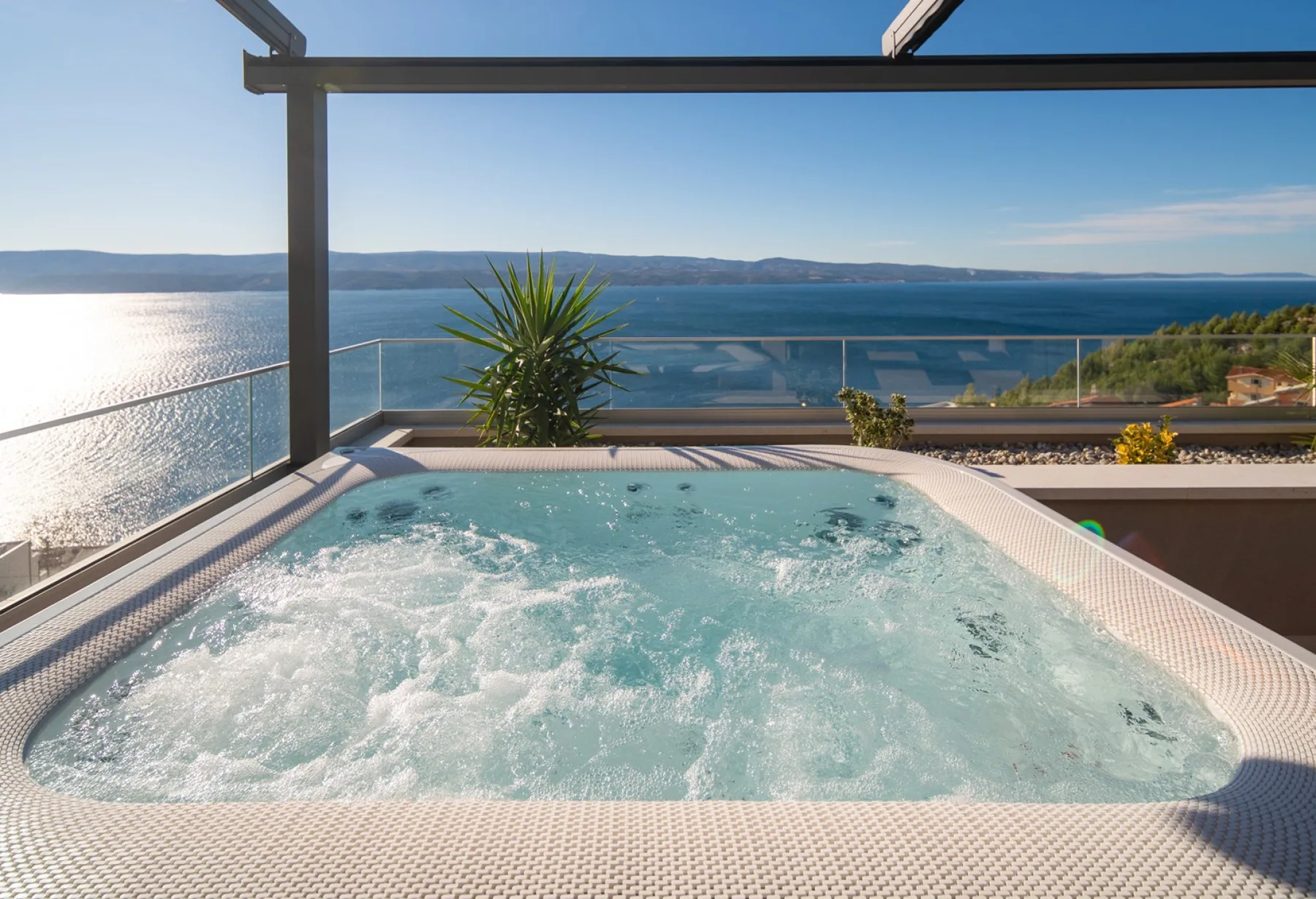 A bubbling hot tub sits on a terrace overlooking the water.