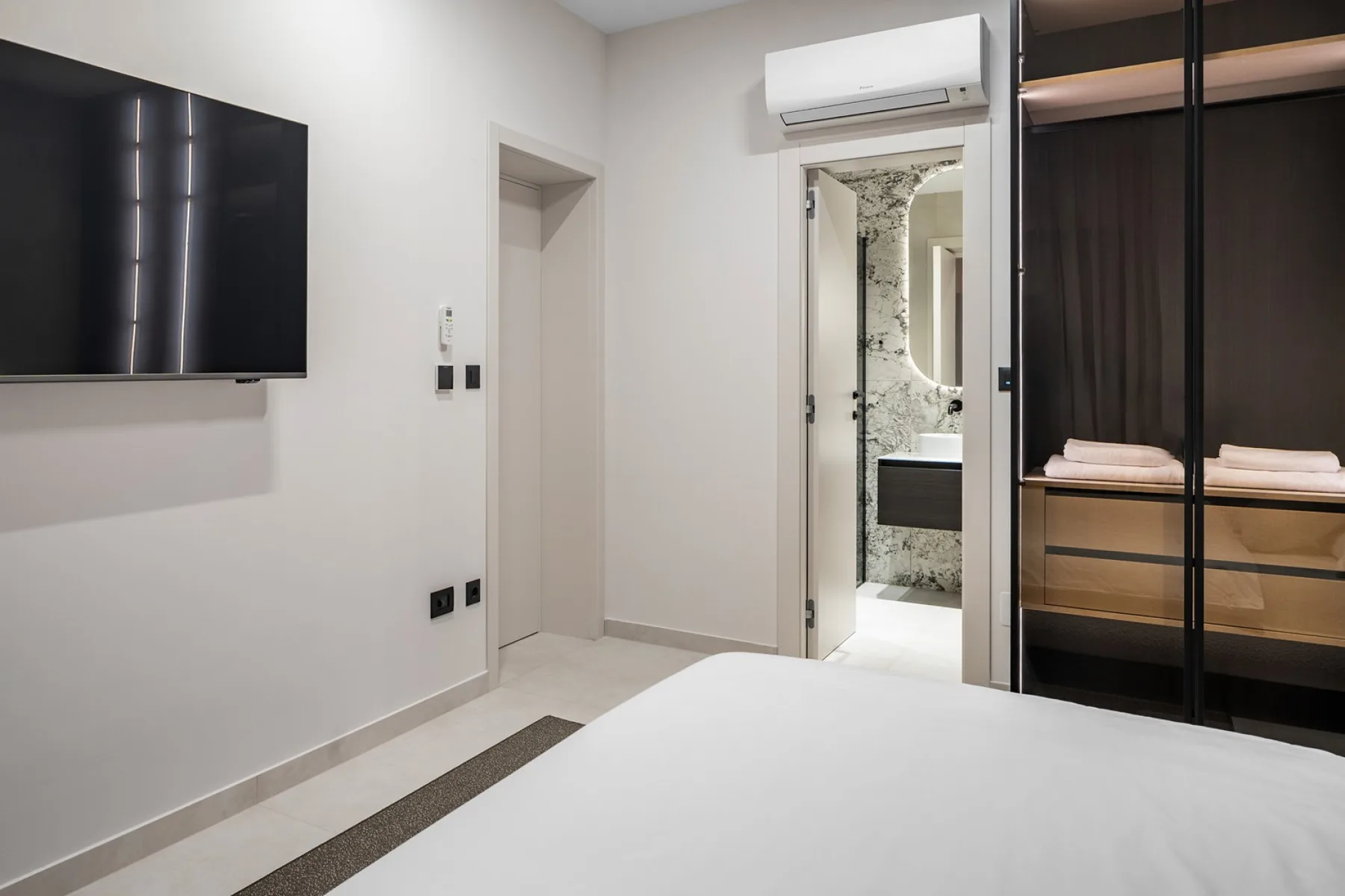 A bedroom with a wall-mounted television and an open bathroom doorway.