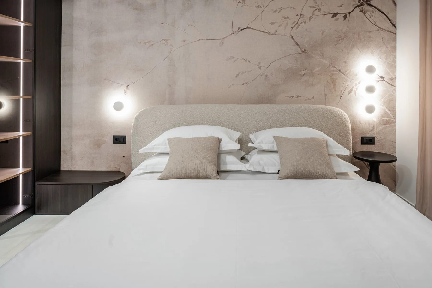 A bedroom with a neatly made bed and soft wall lighting.
