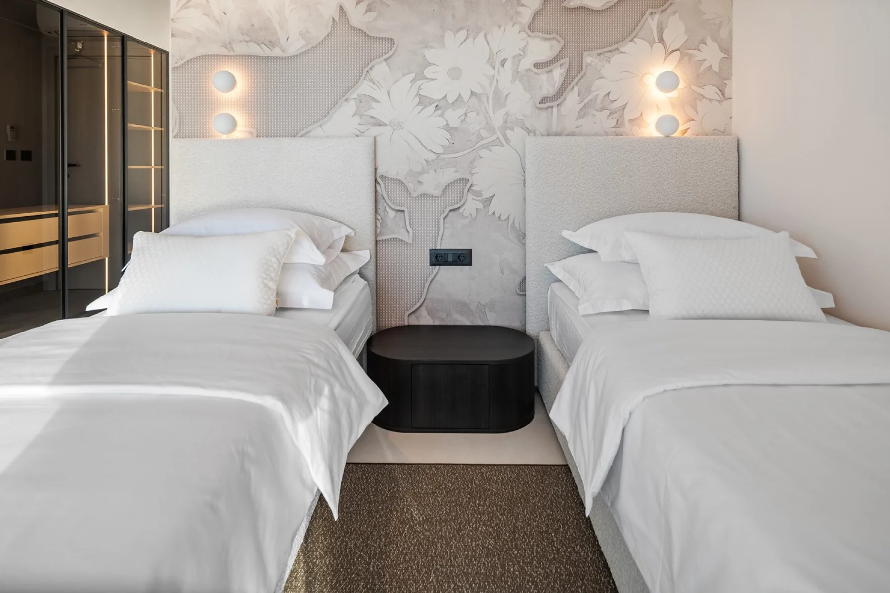A bedroom with two beds, white bedding, and a floral wall mural.