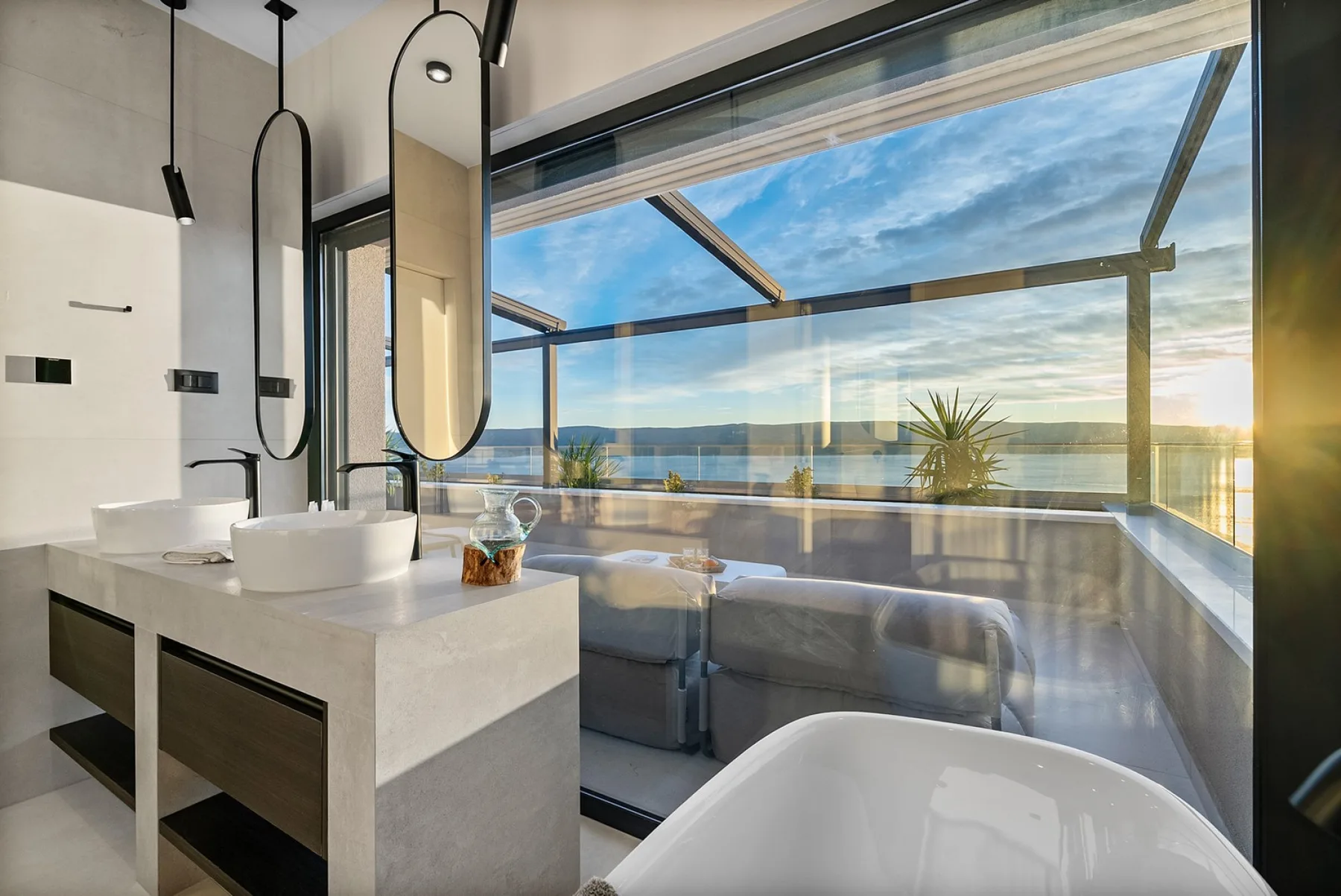 A modern bathroom with a freestanding tub and a glass wall overlooking the sea.