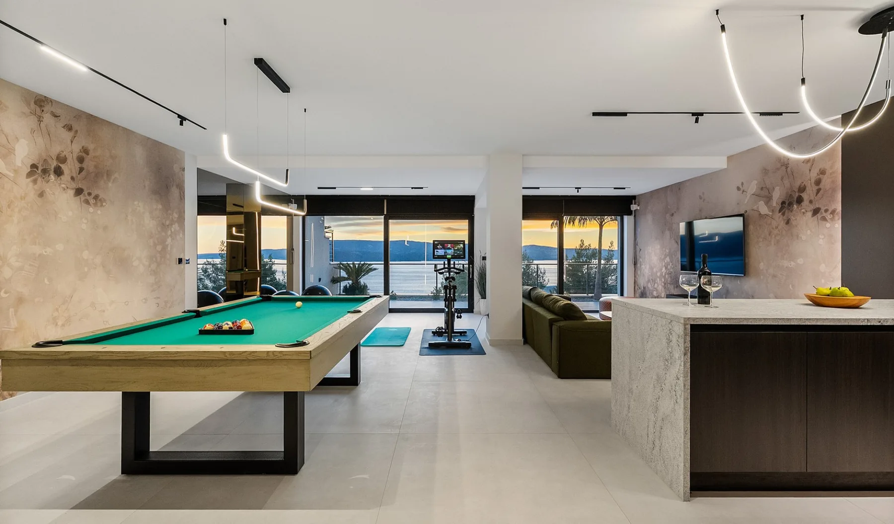 A modern game room with a pool table and a seating area by large windows.