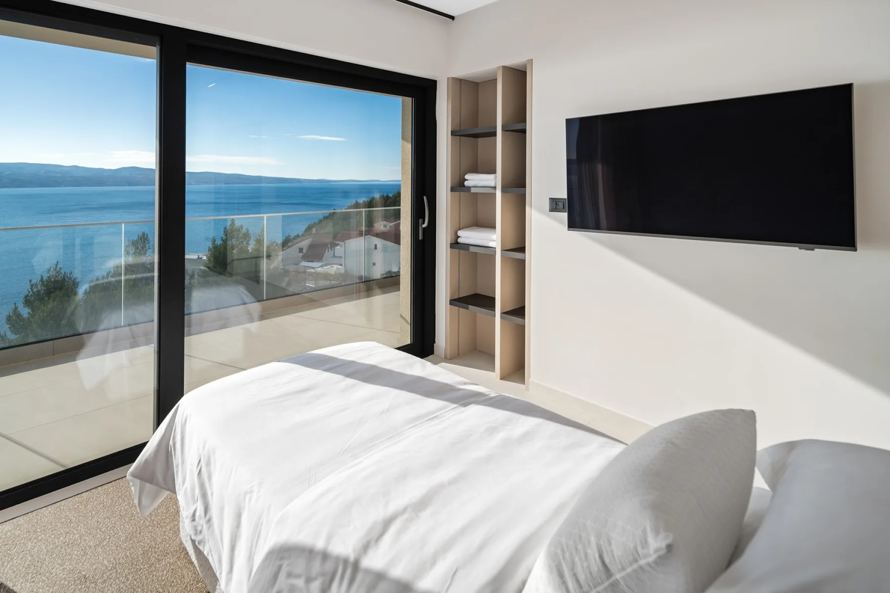 A bedroom with a bed beside large windows overlooking the sea.