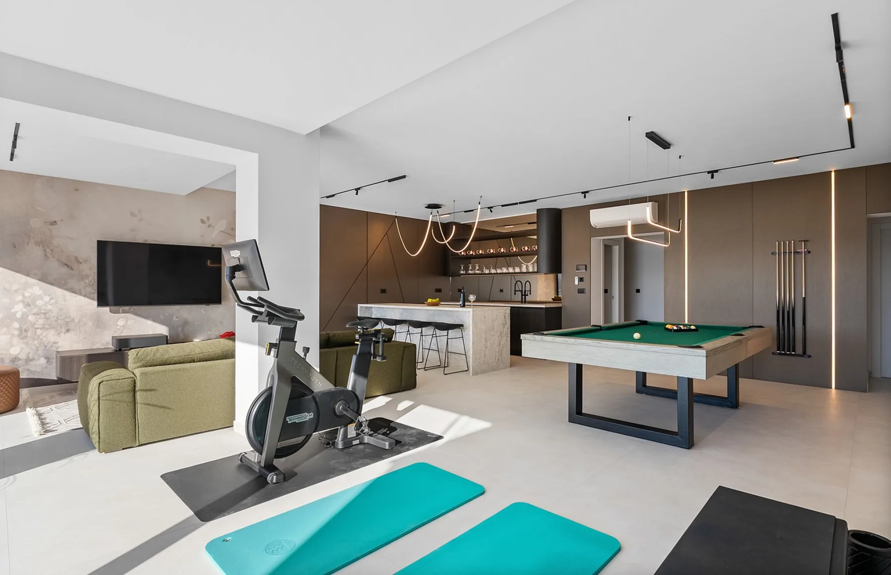 A modern open-plan recreation room with a pool table and exercise equipment.