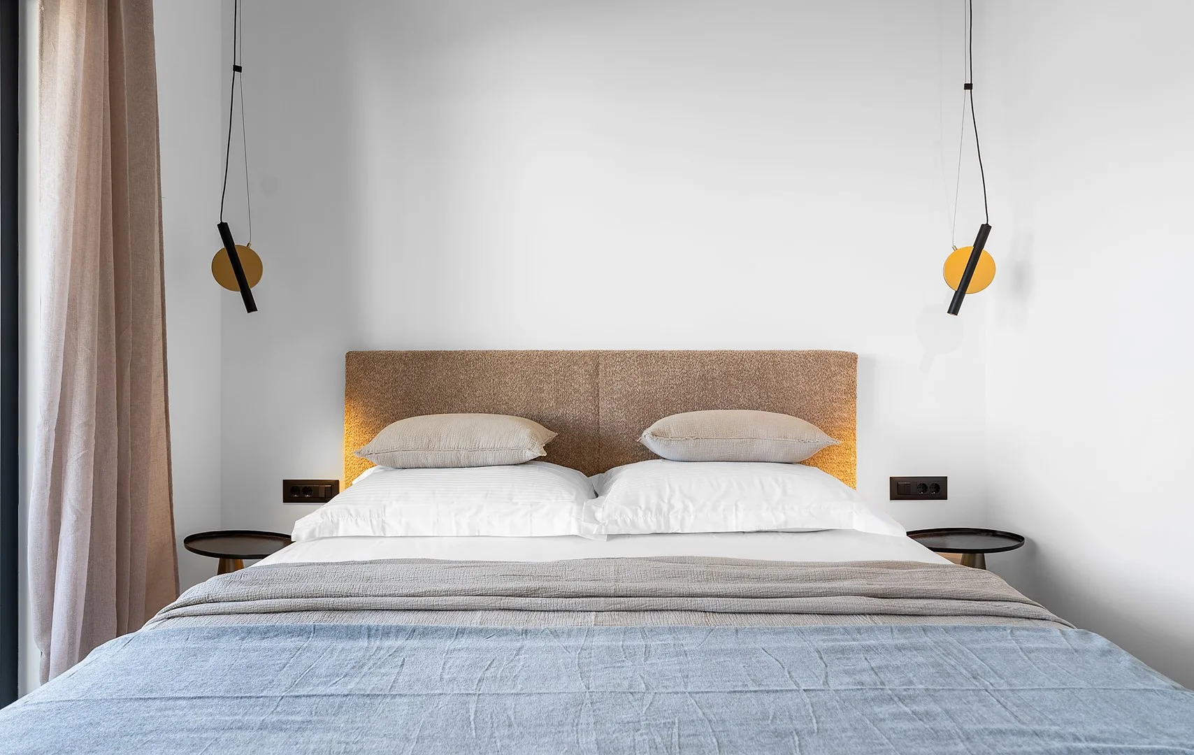 A bedroom with a neatly made bed beneath two hanging lights.