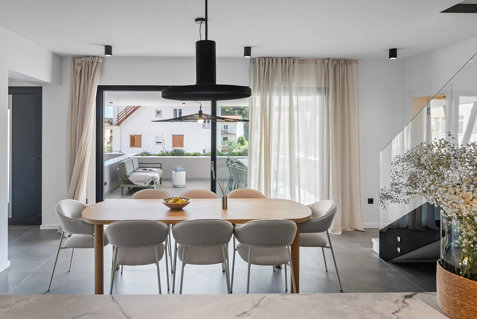 A dining area with a long table and upholstered seating beneath pendant lights.