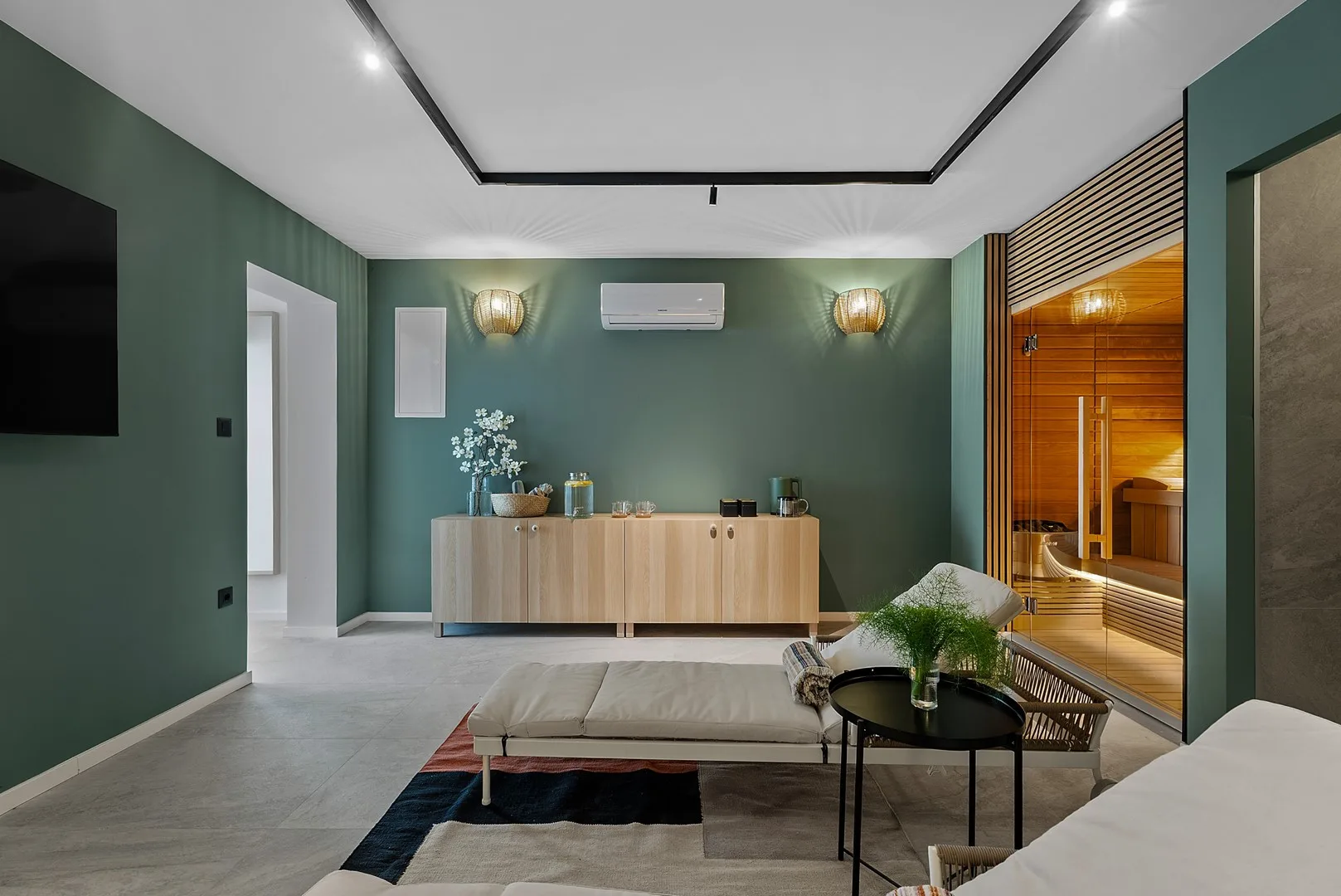 A modern living room with green walls, a low seating area, and warm wood cabinetry.