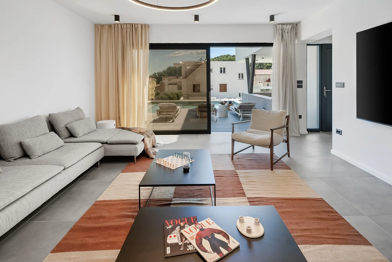 A modern living room with seating, coffee tables, and glass doors opening to a patio.