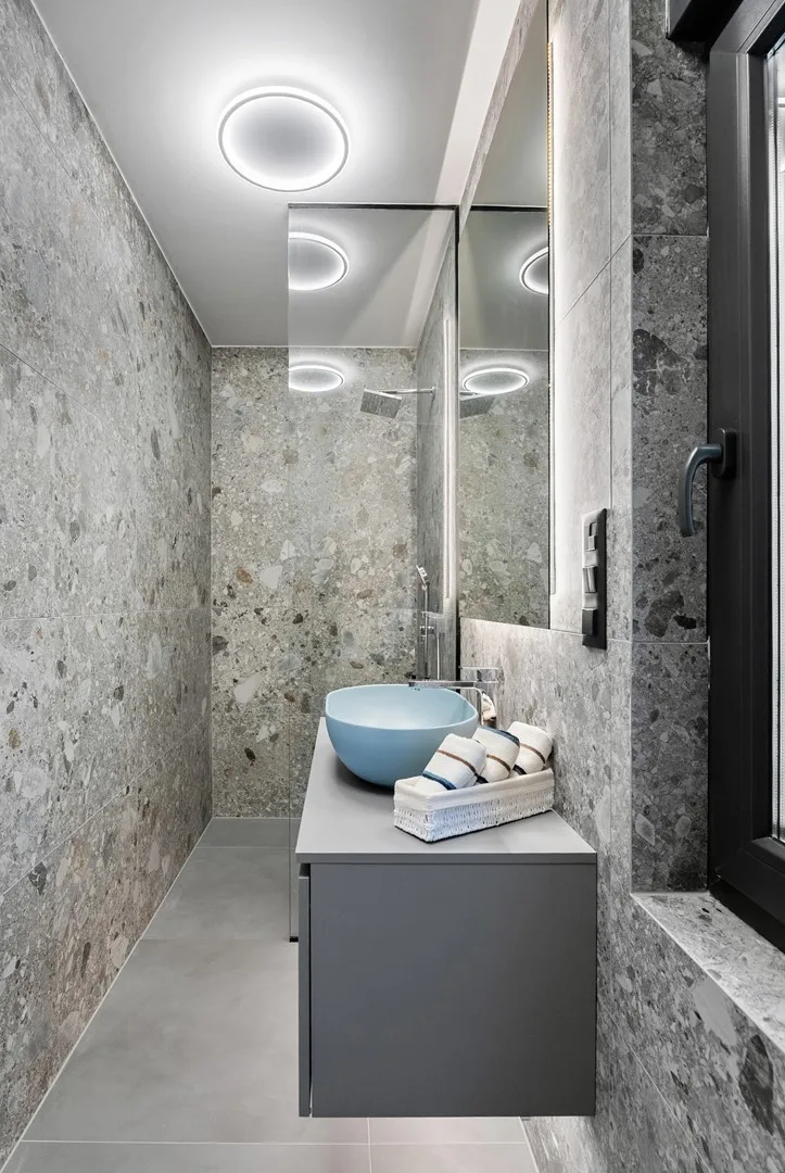 A modern bathroom with a blue vessel sink and gray stone-patterned walls.