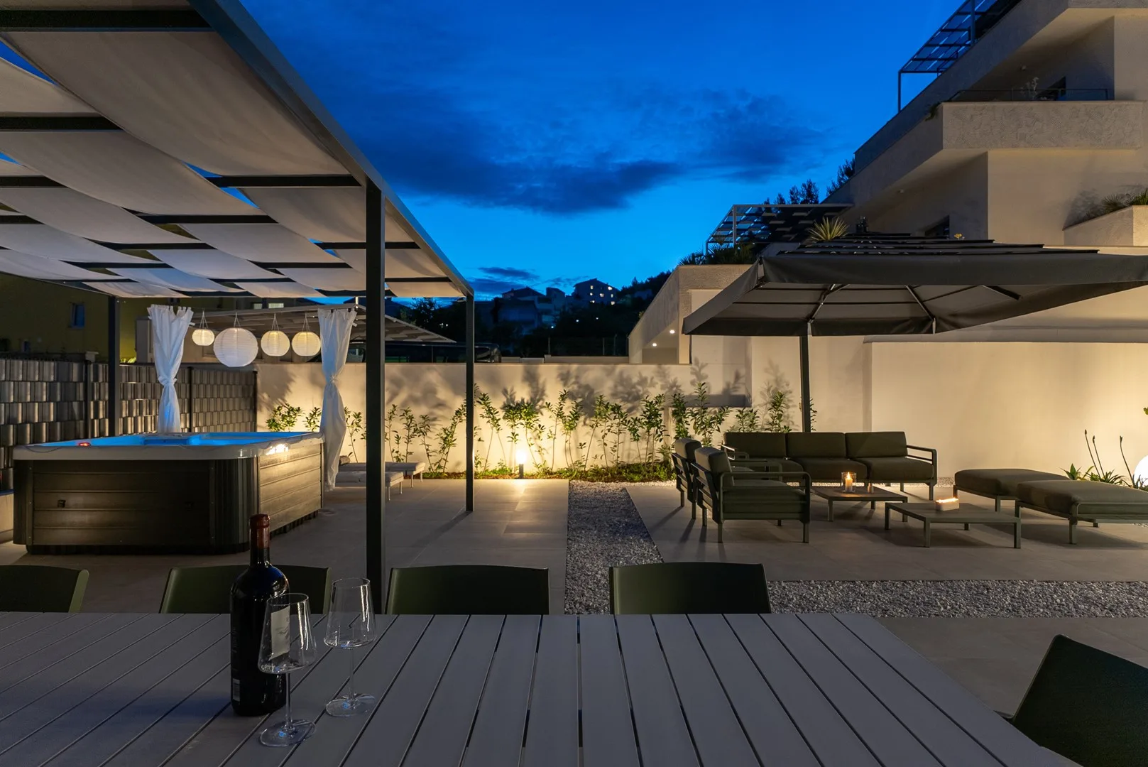 An outdoor terrace at dusk with a hot tub and seating beneath a canopy.