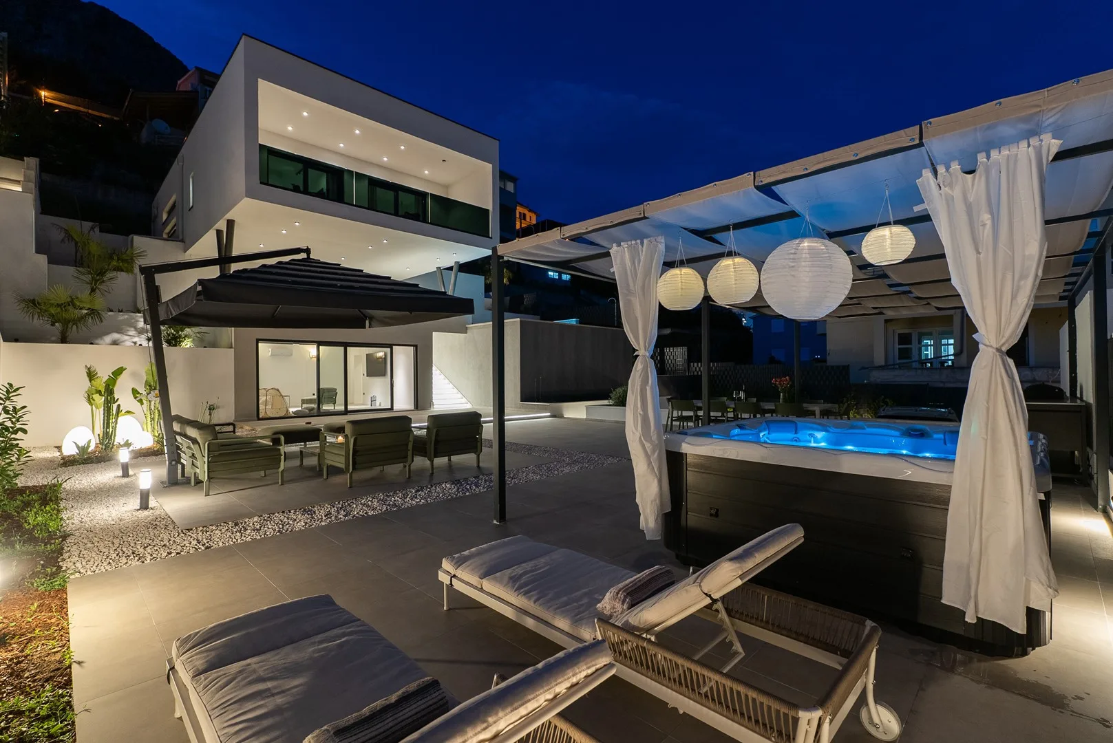 A modern patio at night with lounge seating beside a lit swimming pool.