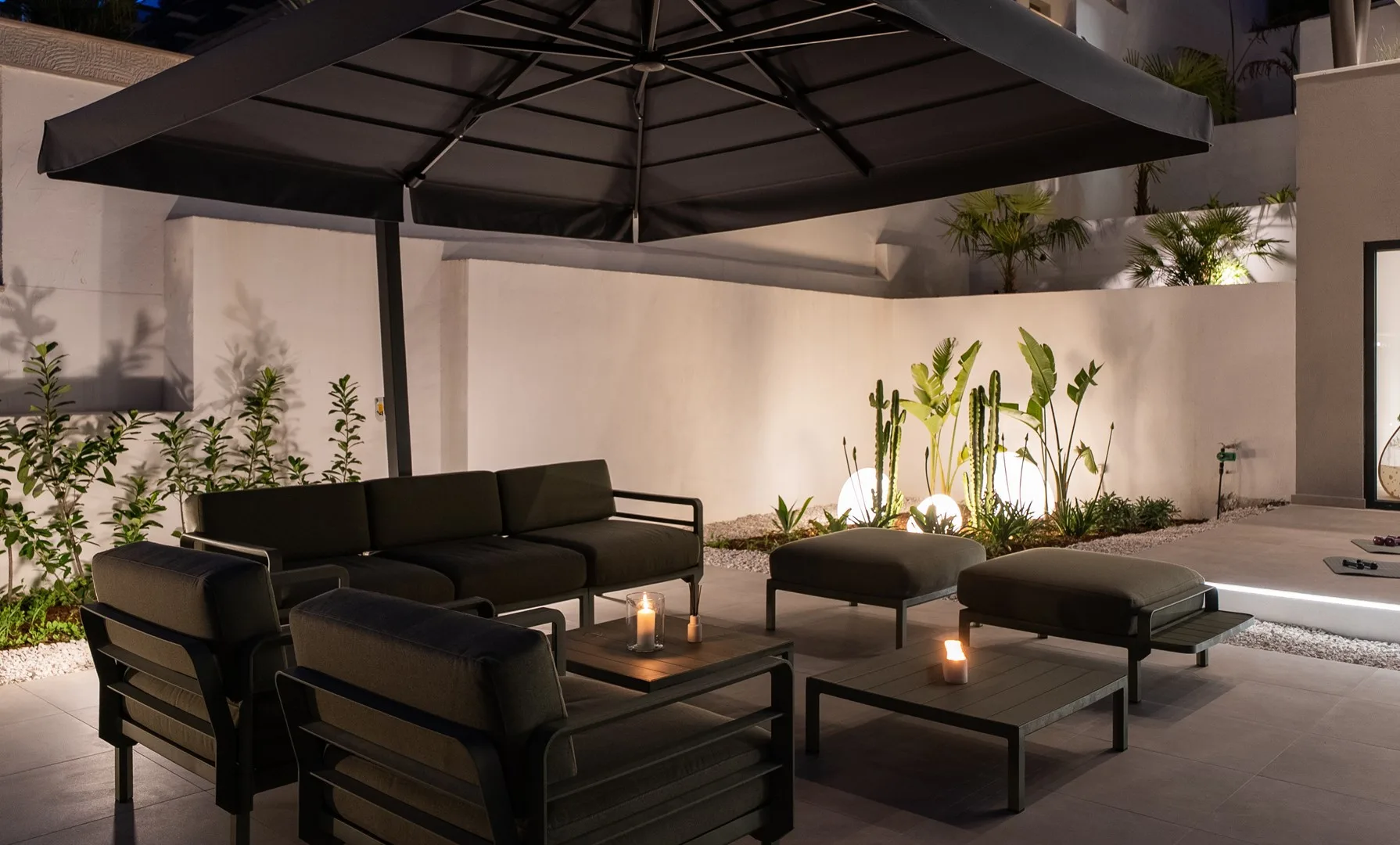 An outdoor patio seating area beneath a large umbrella, with low tables and plants.