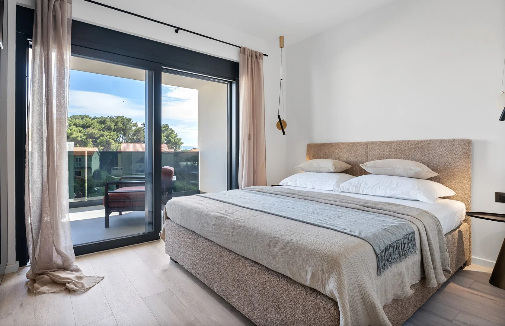 A bright bedroom with a neatly made bed beside large glass doors.