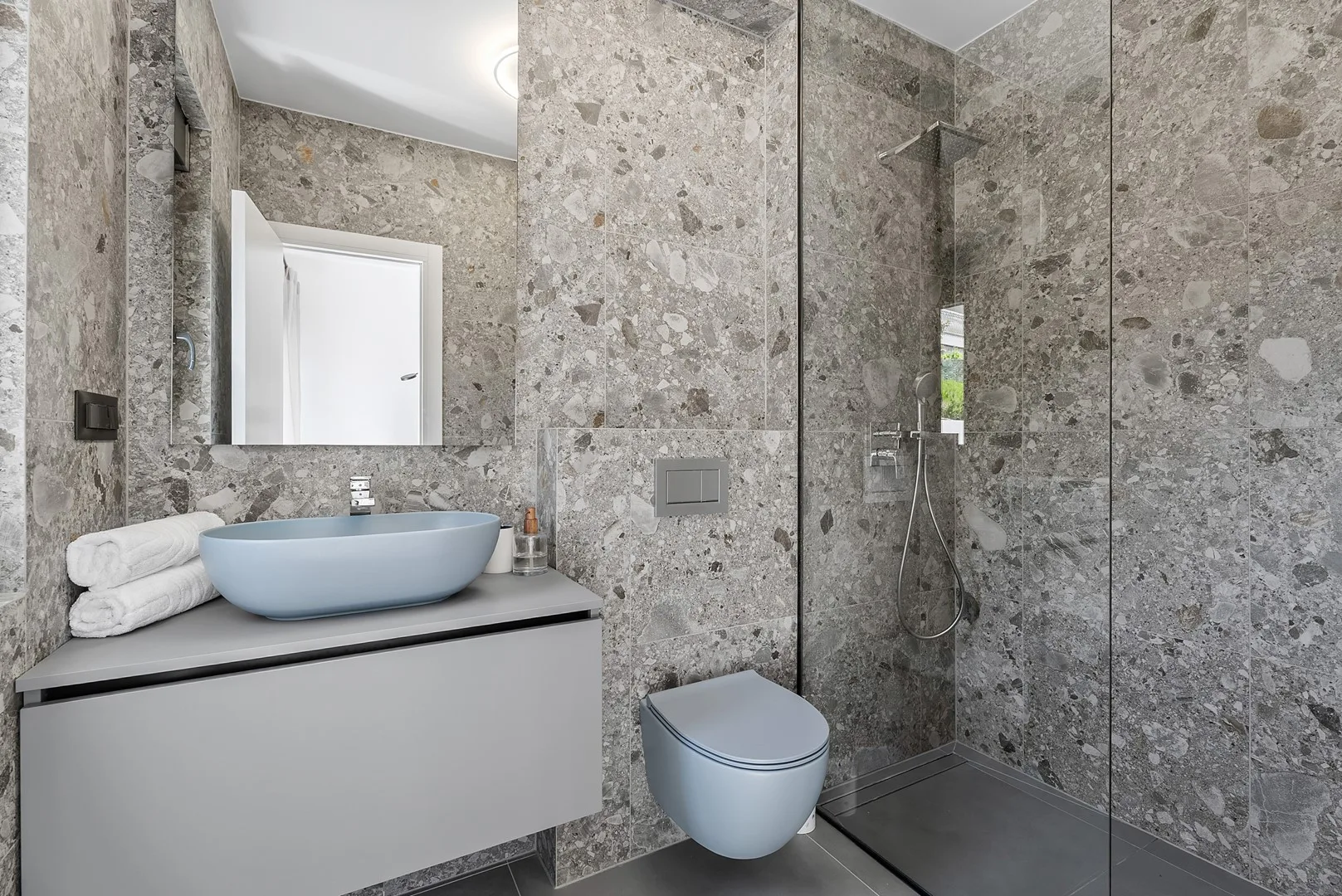 A modern bathroom with a vanity, wall-mounted toilet, and glass-enclosed shower.