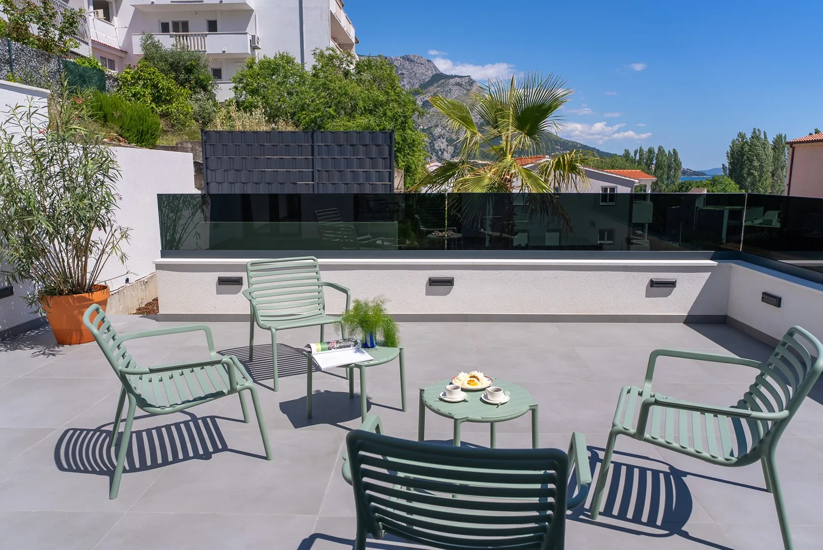 A rooftop terrace with outdoor seating and a small table overlooks greenery and distant hills.