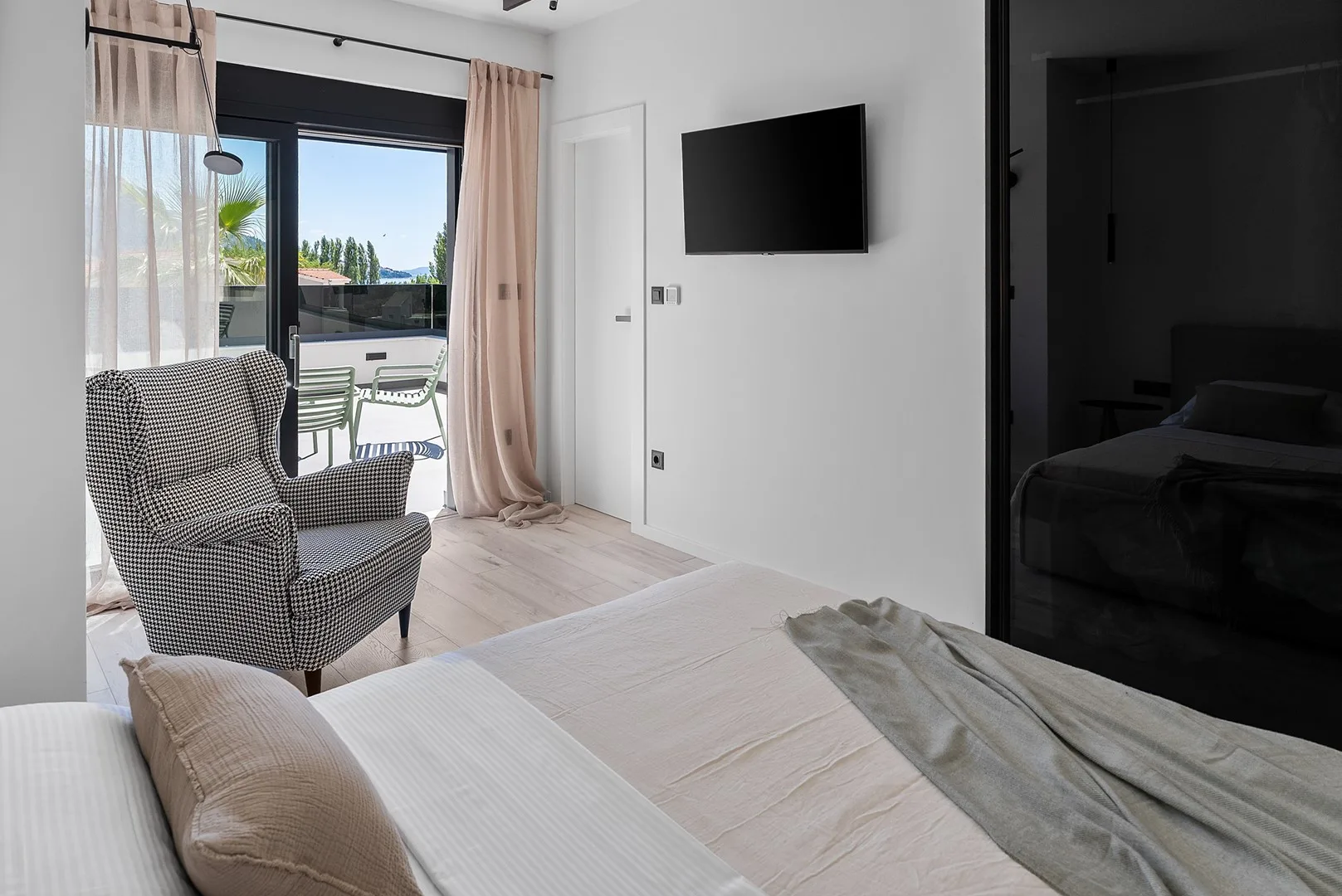 A bright bedroom with a bed, an armchair, and a wall-mounted television.