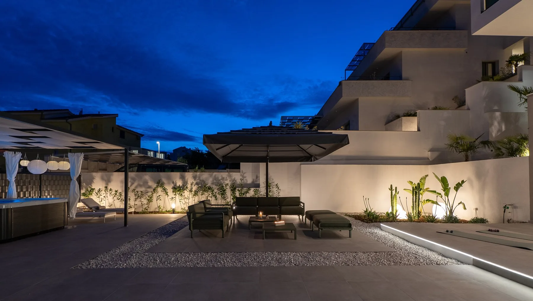 An outdoor patio with seating and large umbrellas beside a lit building at dusk.