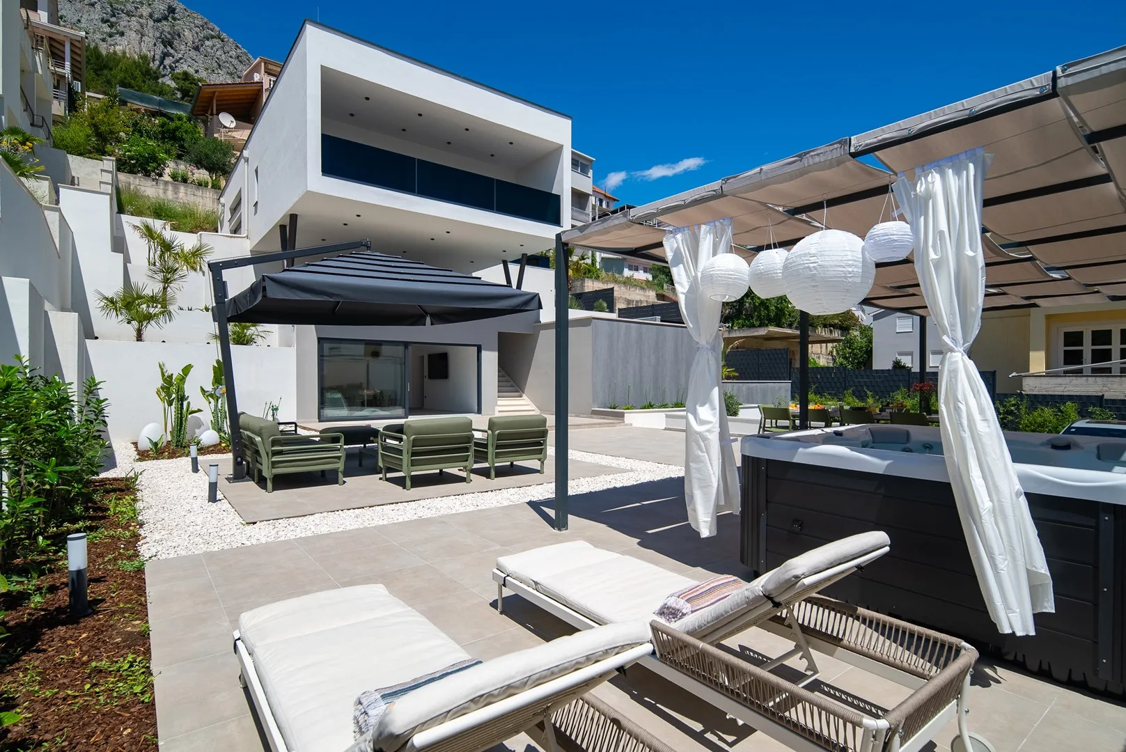 An outdoor patio with lounge seating, a shade canopy, and a hot tub.