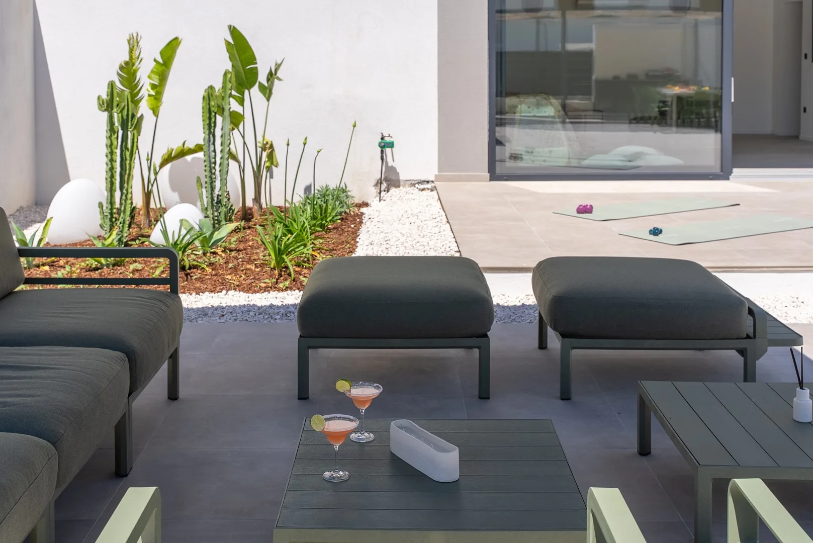 An outdoor patio seating area faces a glass door and planted garden.