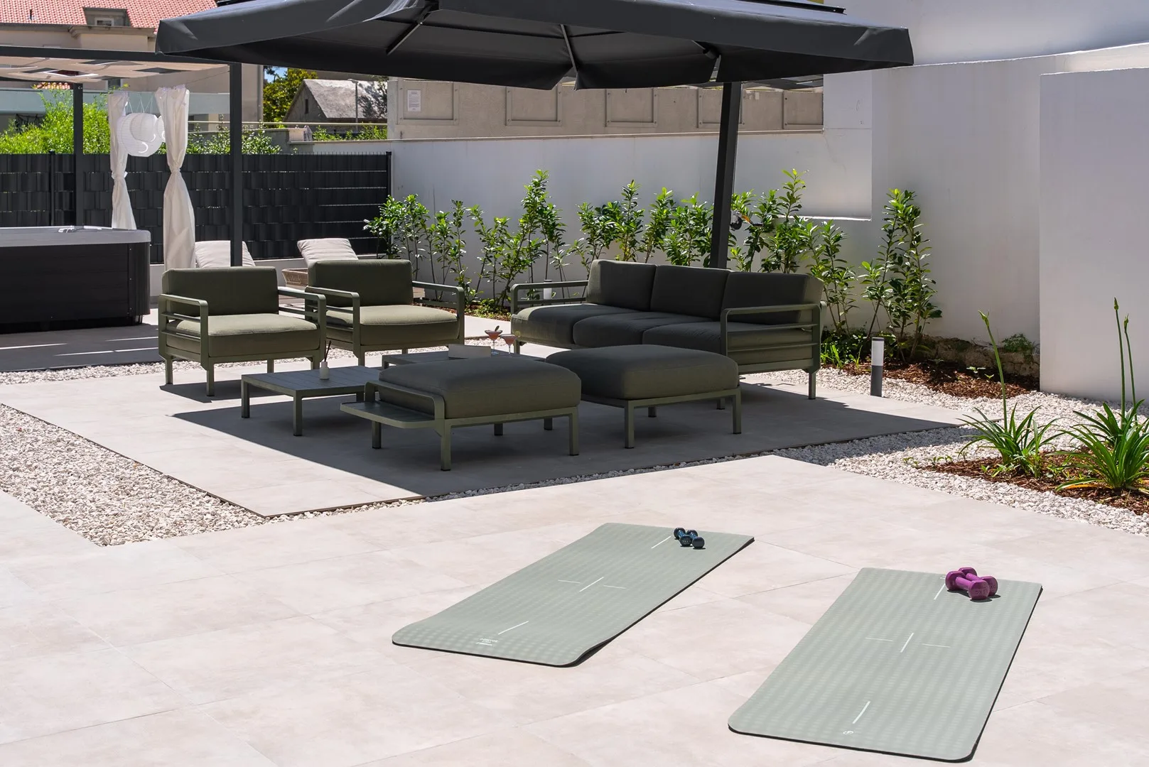 An outdoor patio with lounge seating, a large umbrella, and exercise mats.