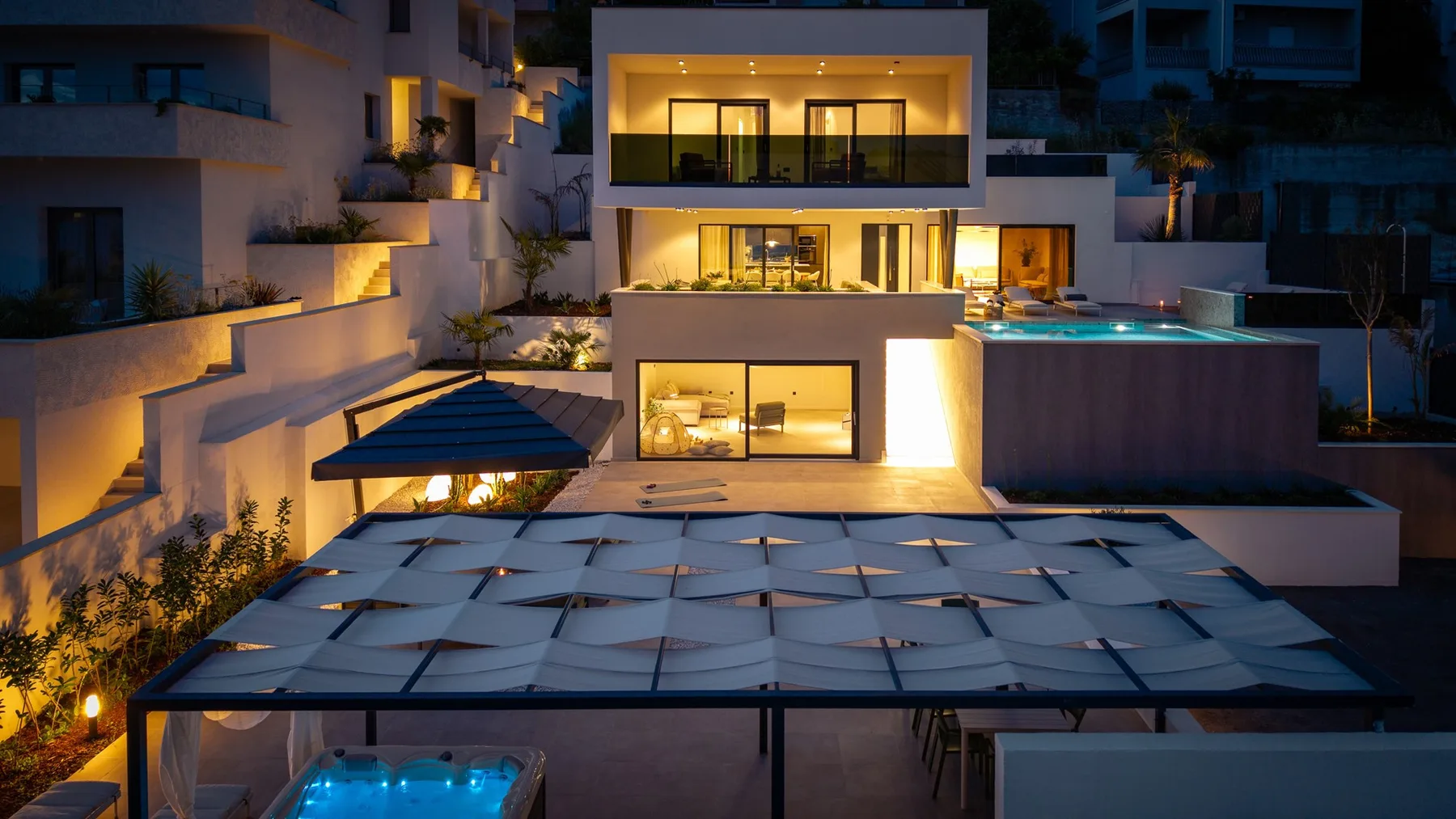A modern building at night, with illuminated windows and a swimming pool.