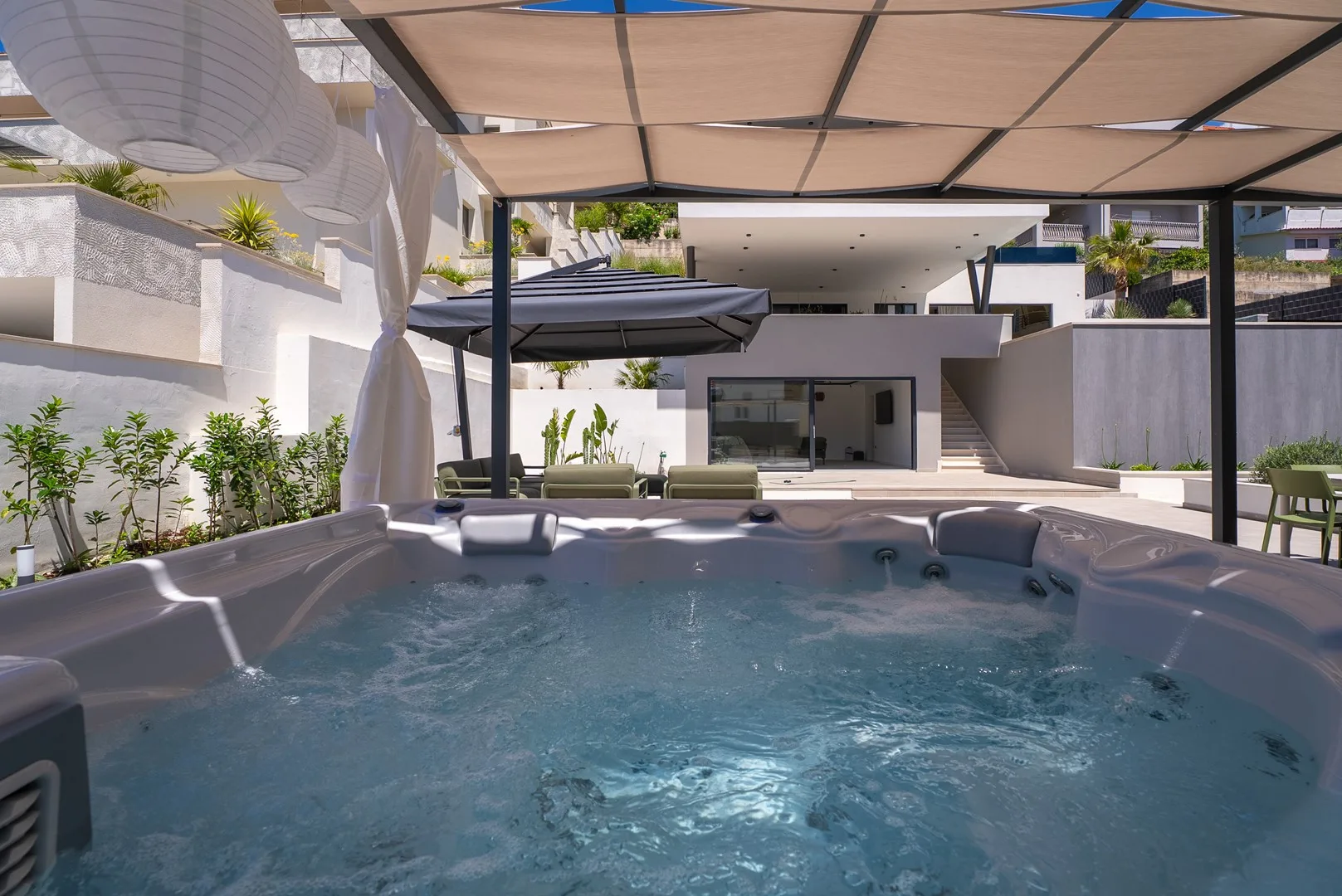 An outdoor hot tub sits beneath a shade canopy beside a modern building.