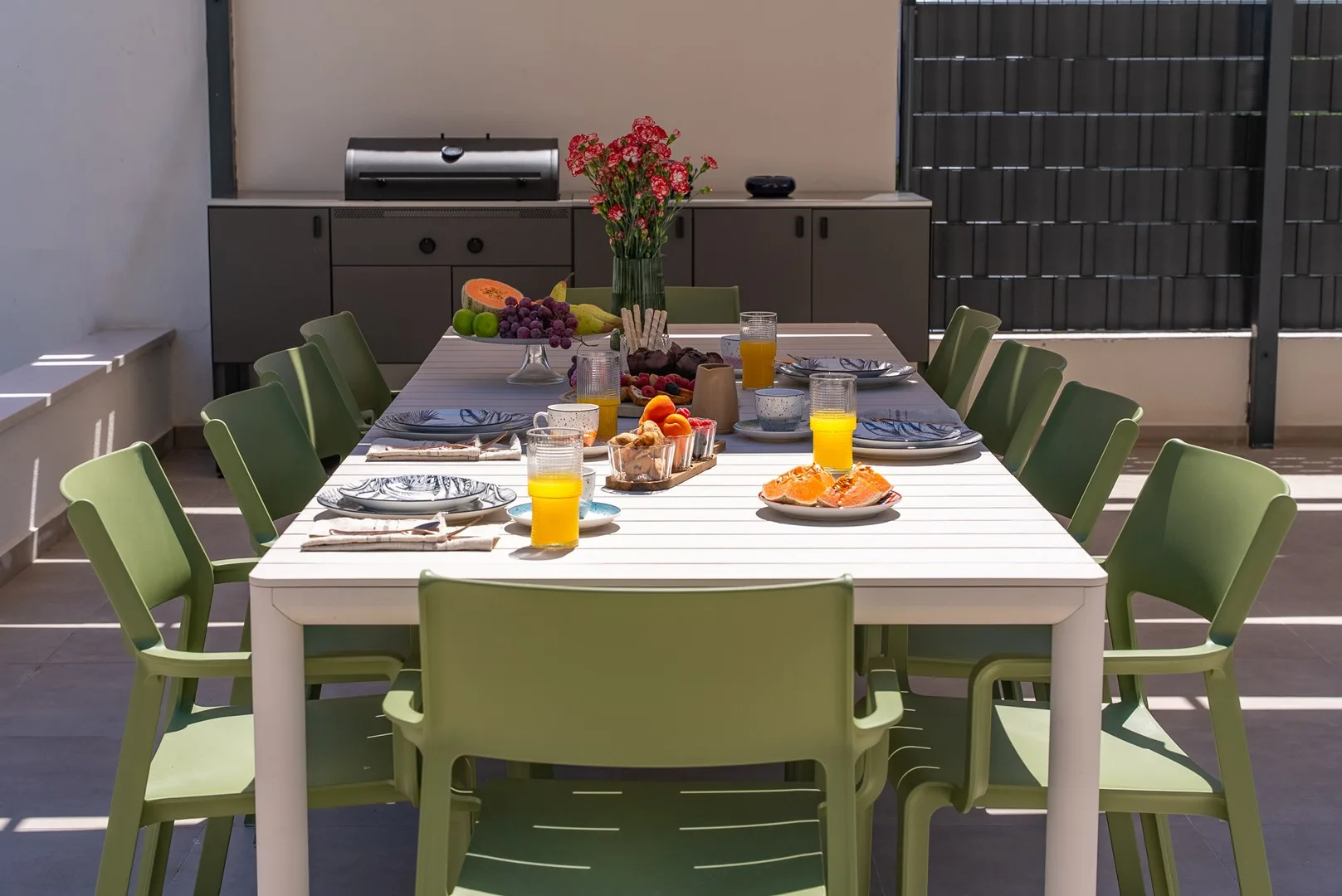 An outdoor dining area with a long table set with plates, glasses, and flowers.