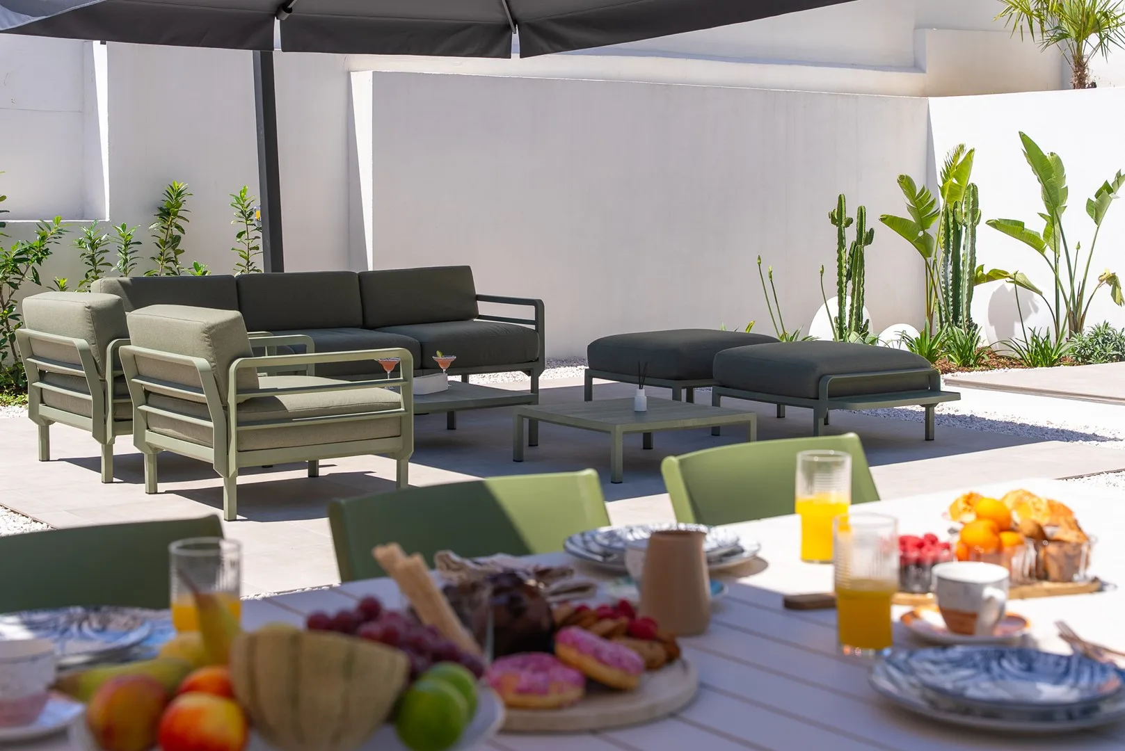 An outdoor patio seating area with a low table and a spread of food in the foreground.