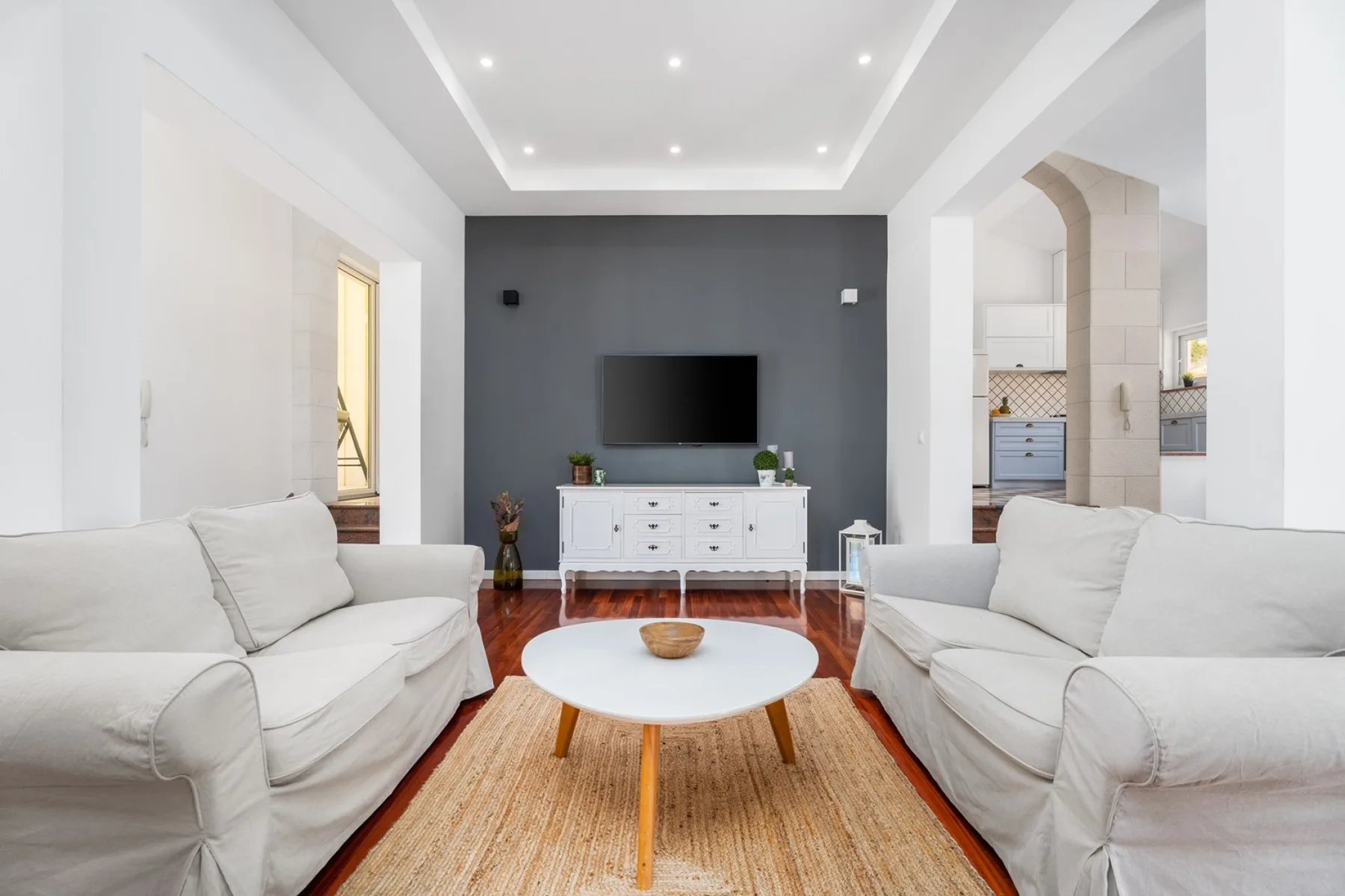 Una sala luminosa tiene asientos blancos, una mesa redonda y un televisor.