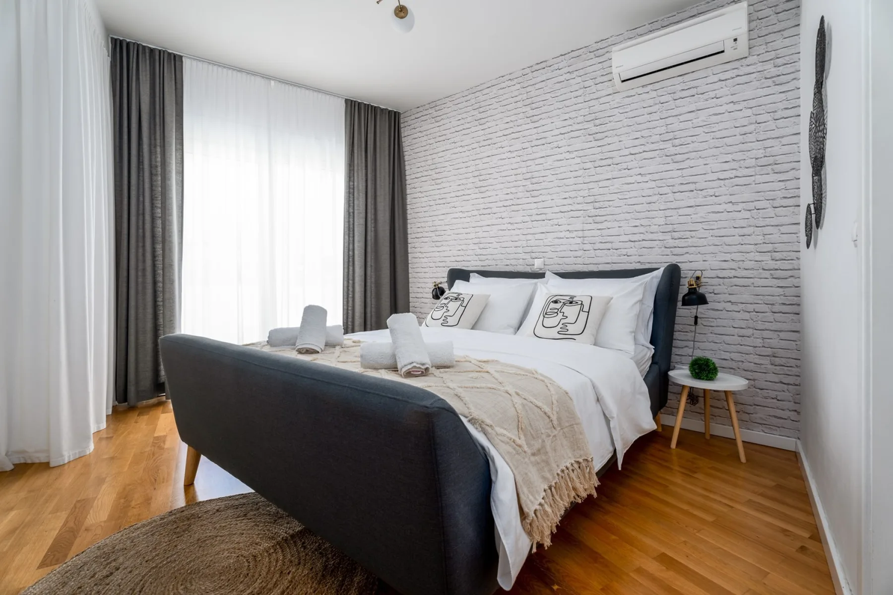 Un dormitorio con una cama, asientos oscuros y una gran ventana con cortinas.