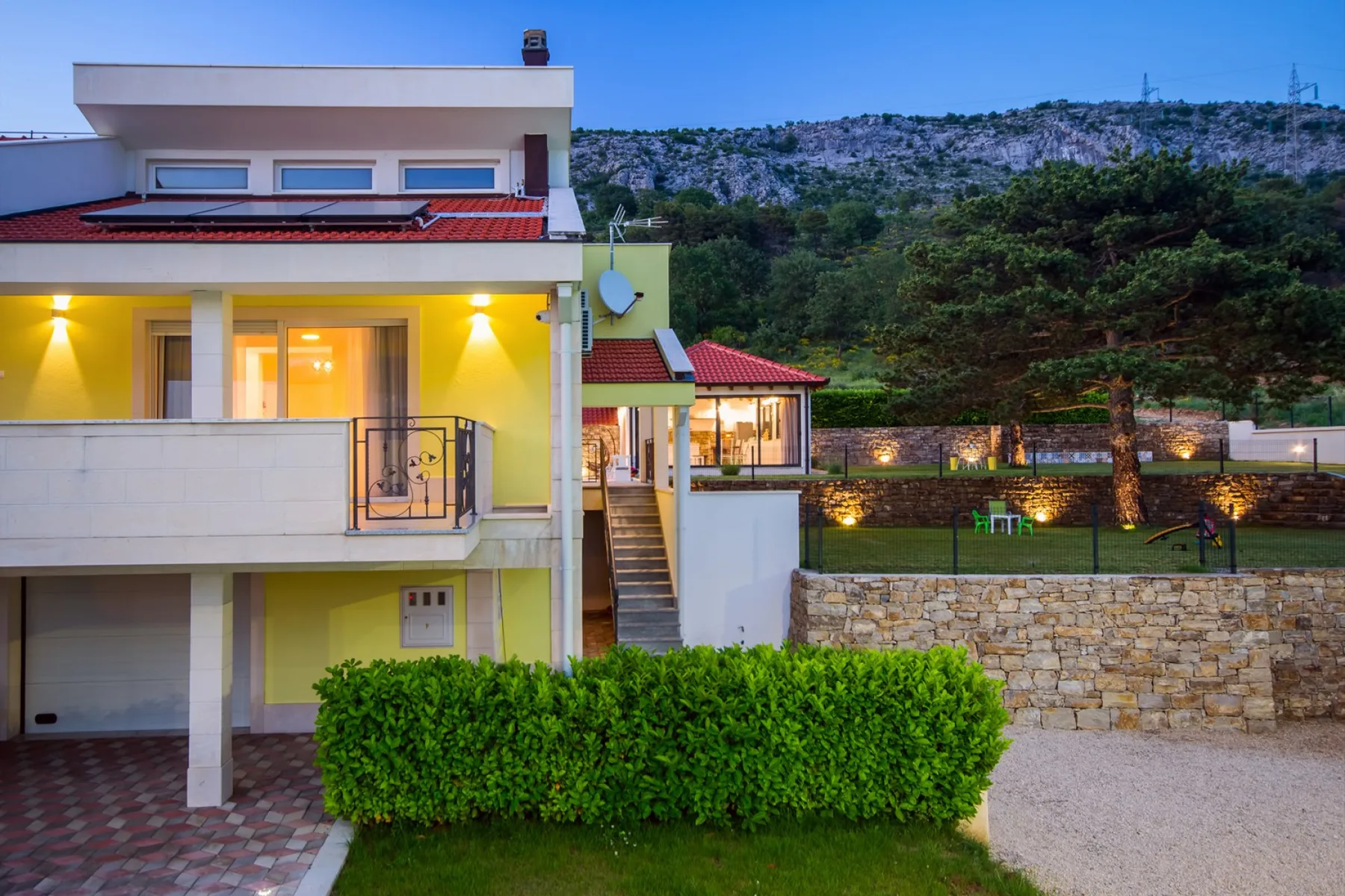 Una casa moderna de varios pisos con balcones iluminados y un jardín cuidado.