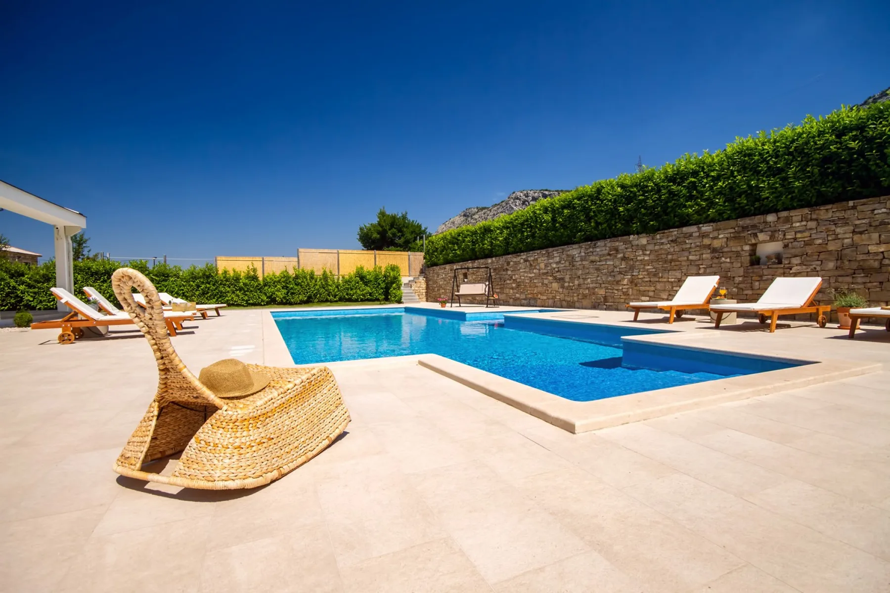 Una zona de piscina al aire libre con asientos junto a un muro de piedra.