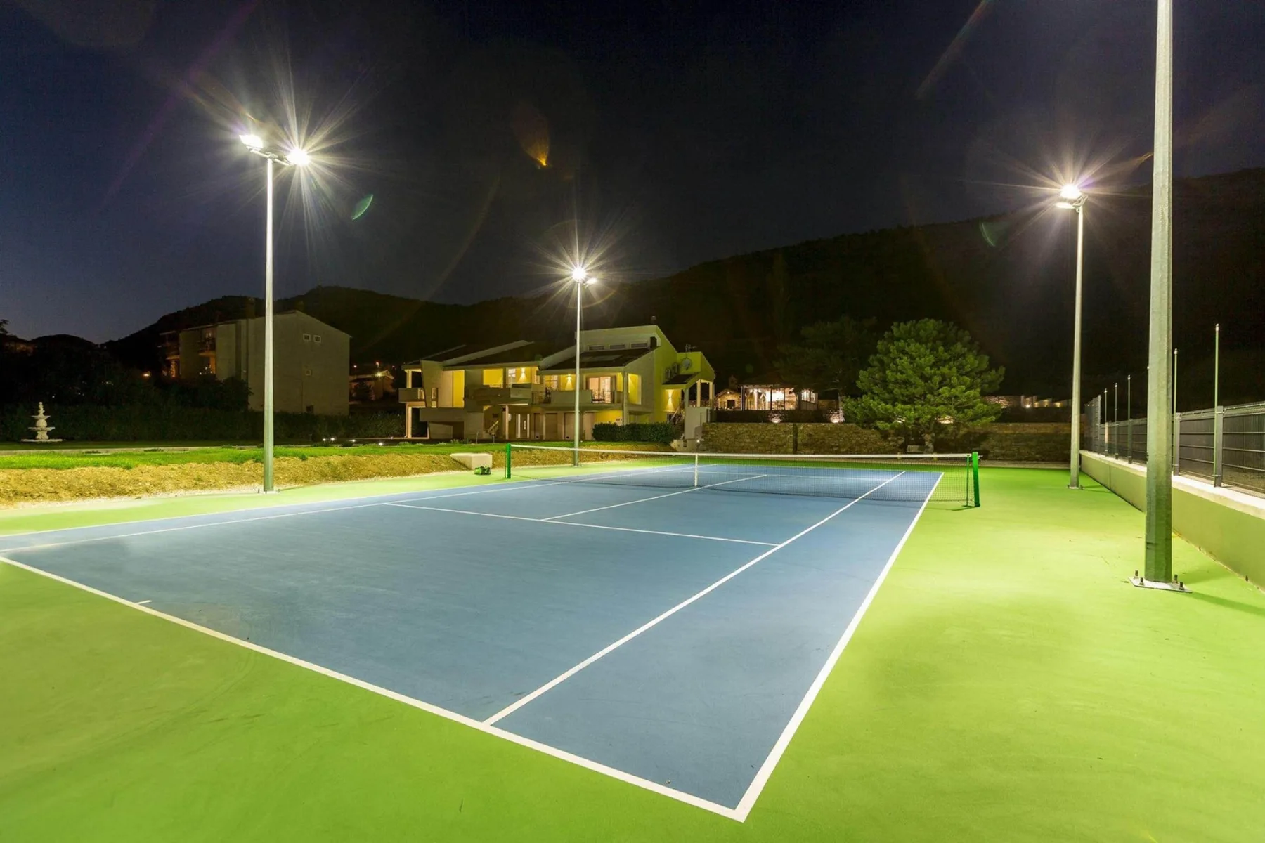Una cancha de tenis al aire libre de noche, iluminada por reflectores altos.
