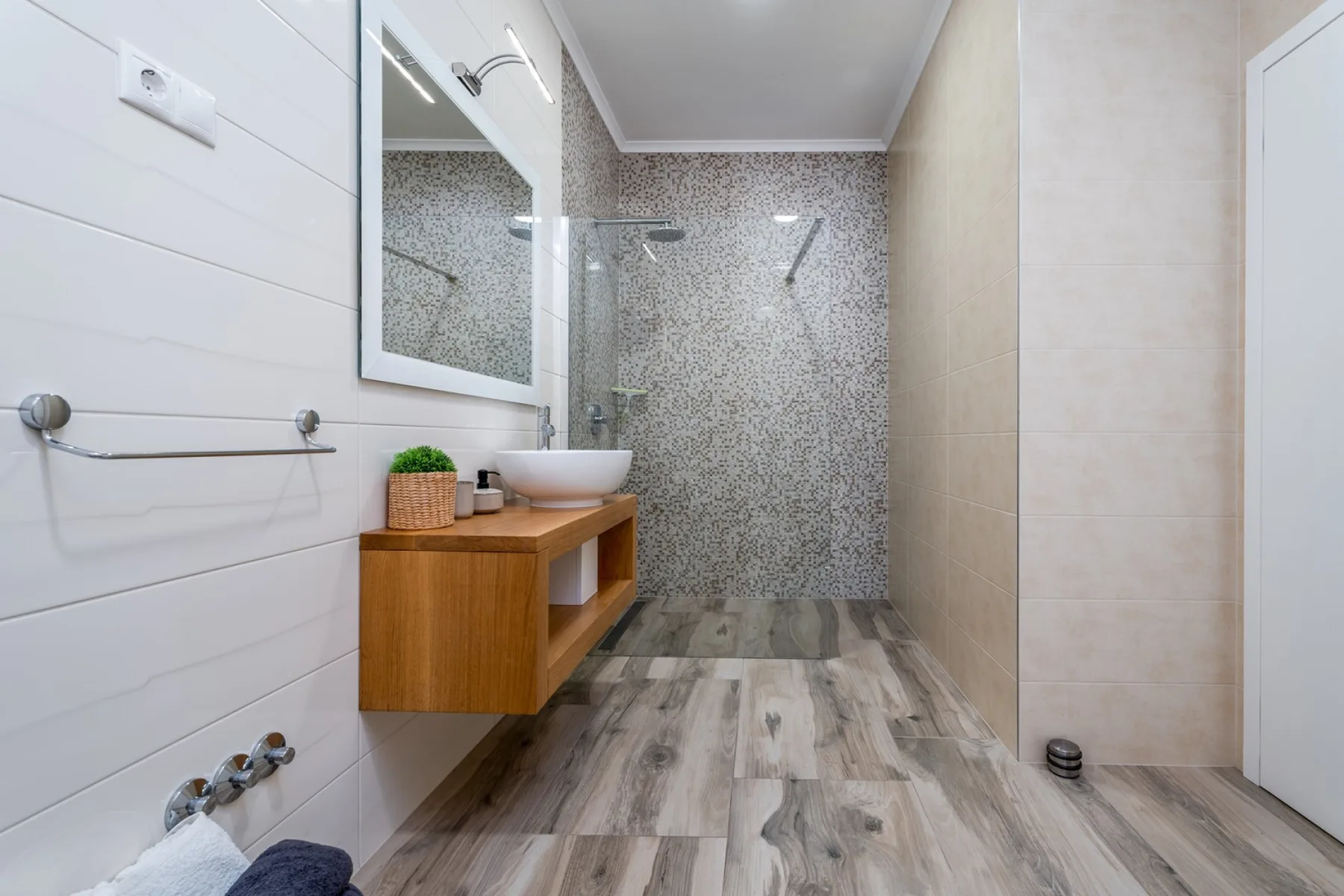 Un baño moderno con ducha de cristal y un mueble de lavabo de madera suspendido.