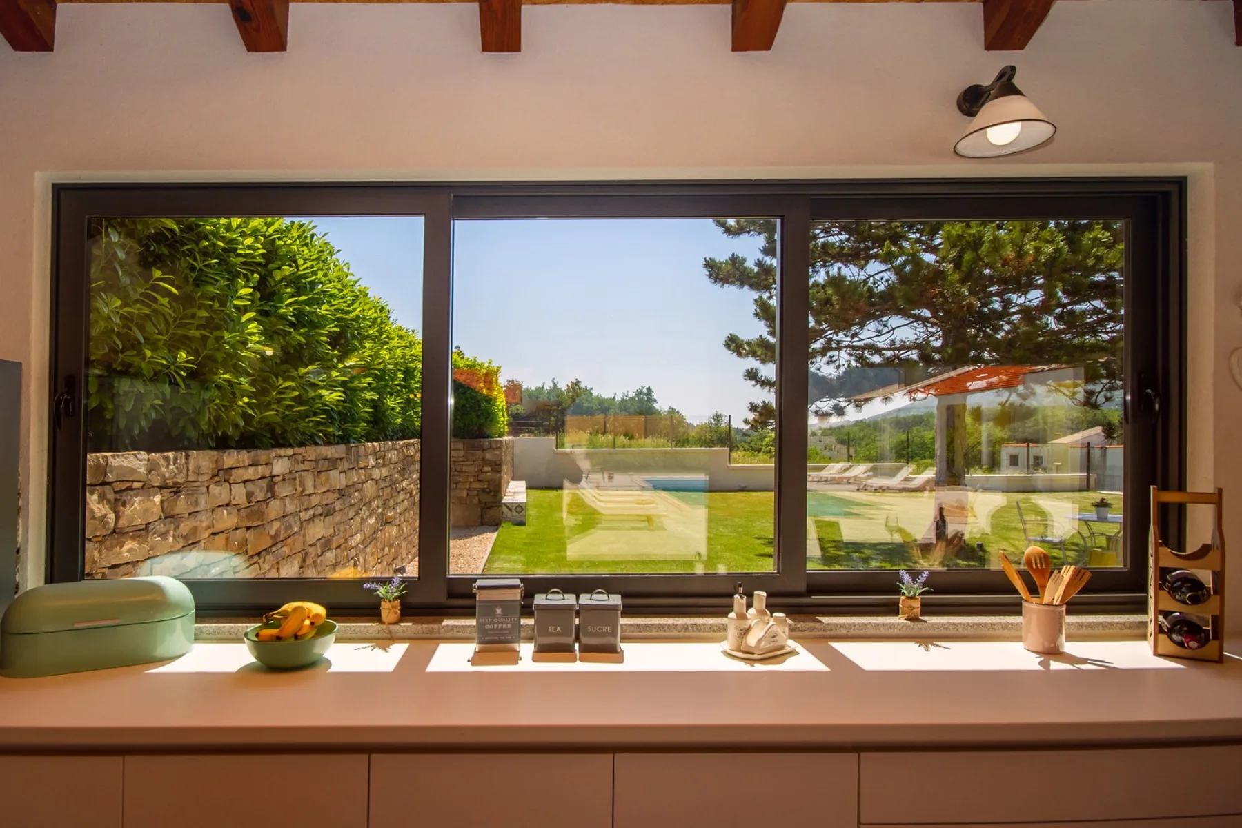 Una ventana amplia da a un césped verde, un jardín y una piscina.