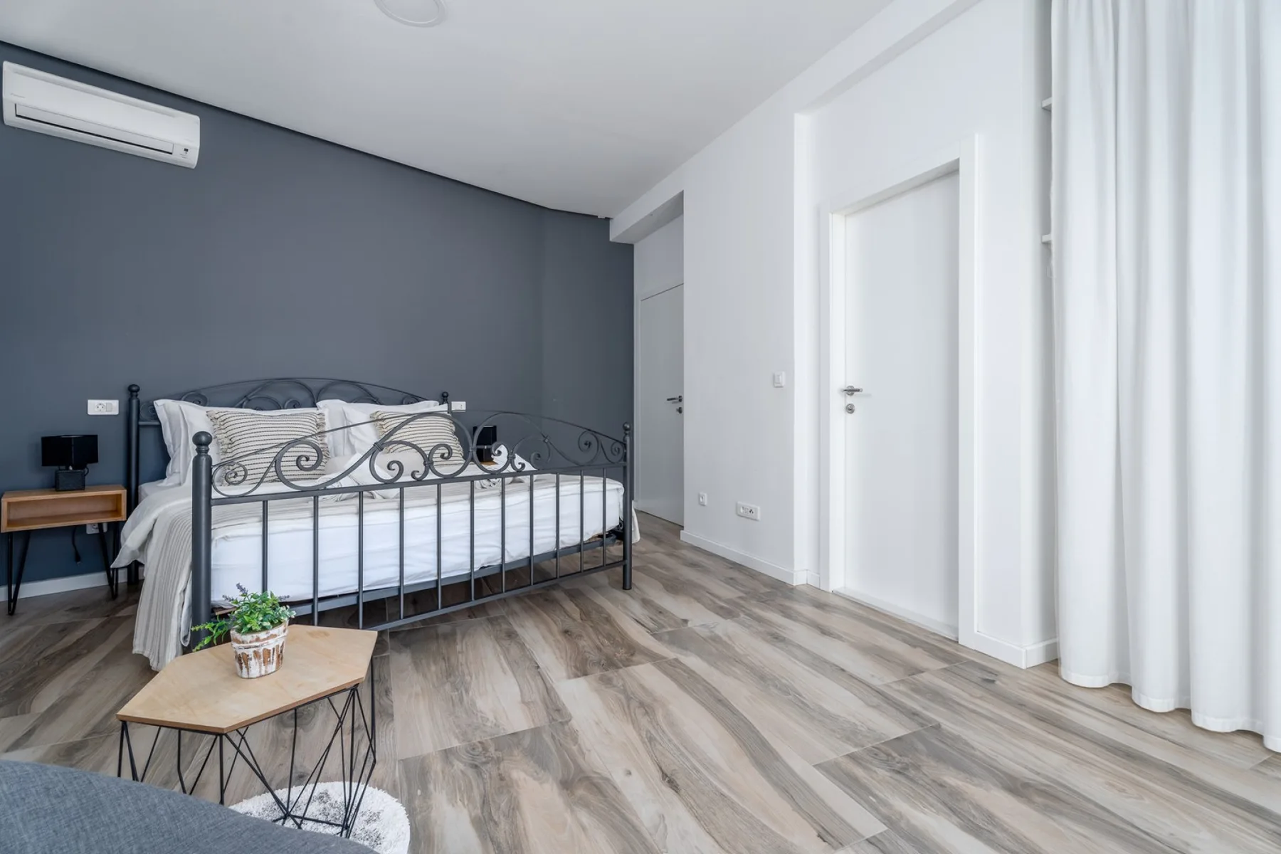 Un dormitorio con una cama de metal y cortinas claras.