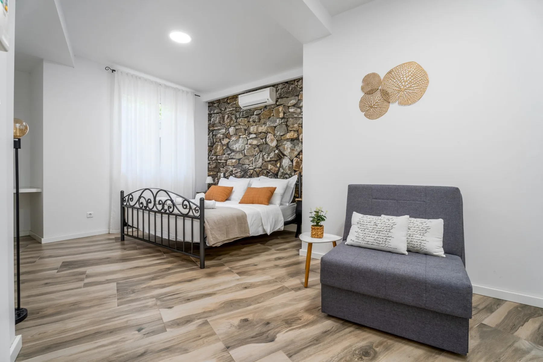 Dormitorio con una cama de estructura metálica y un asiento tapizado gris.