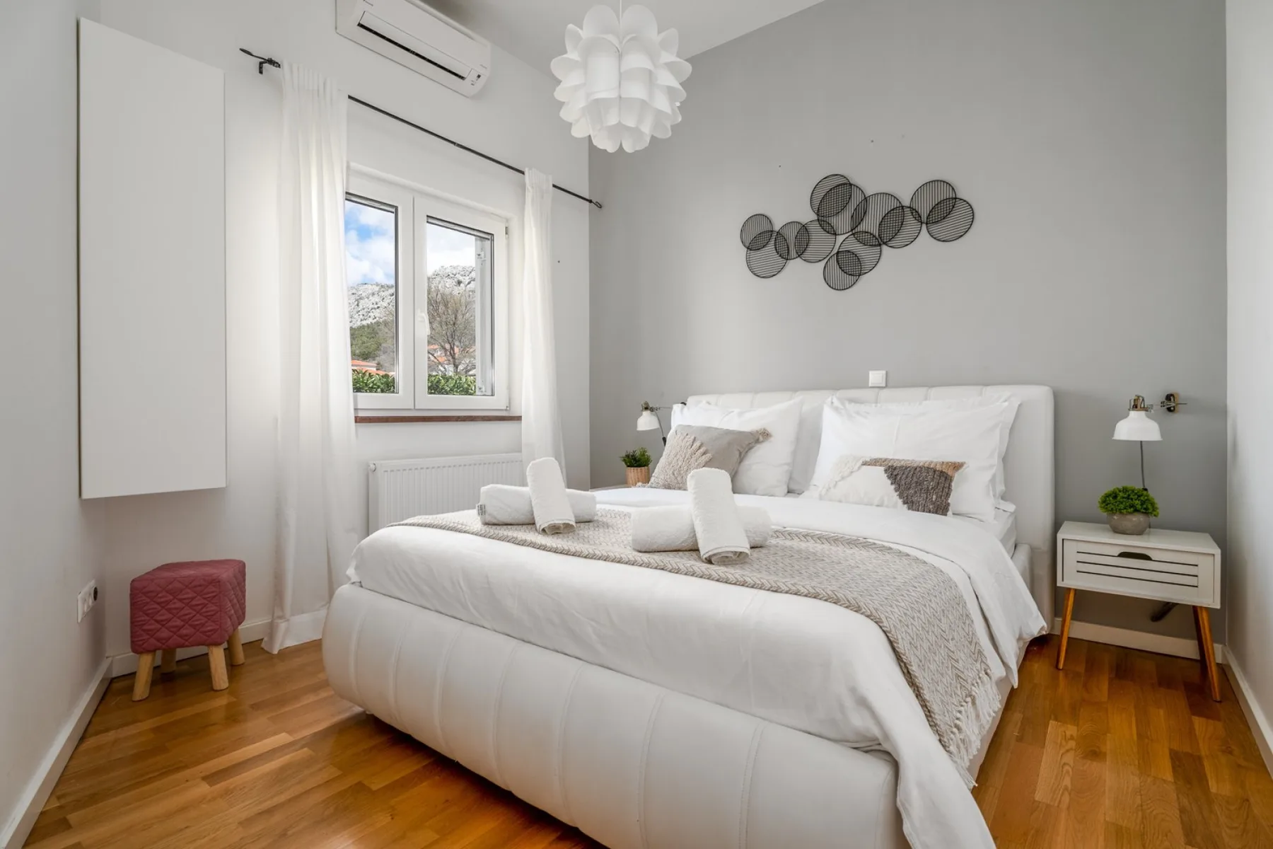Un dormitorio luminoso con una cama blanca, una mesita de noche y una ventana.