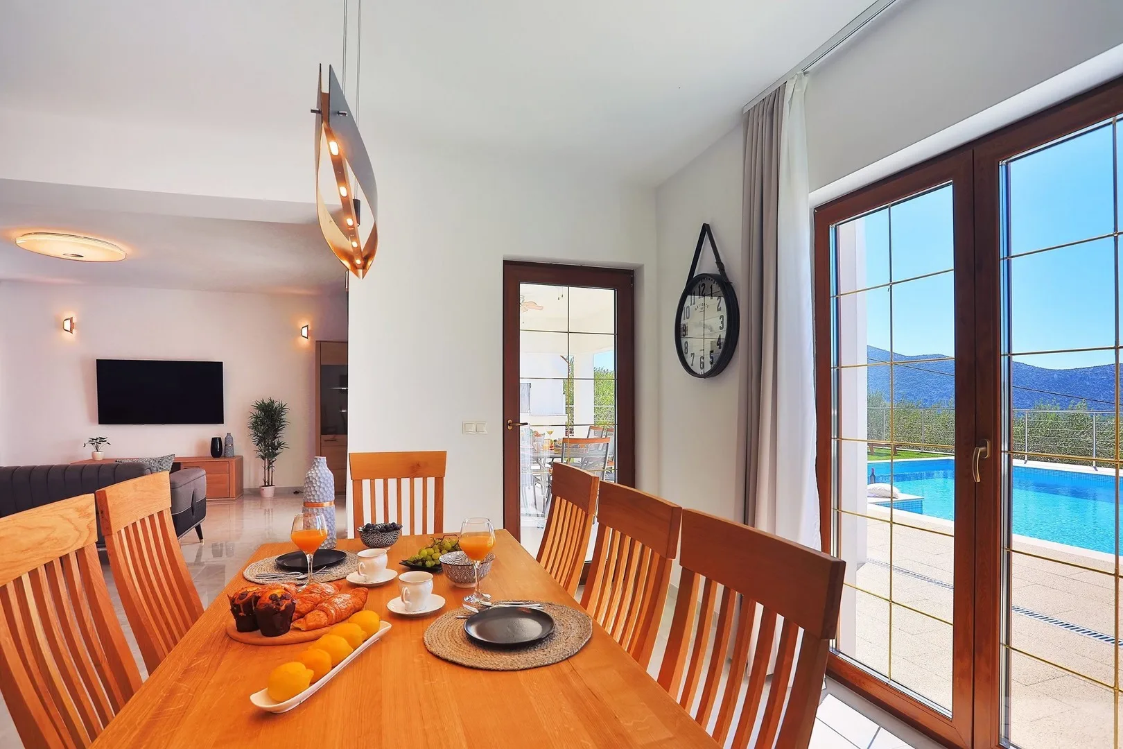 A dining area with a wooden table set beside large windows overlooking a pool.