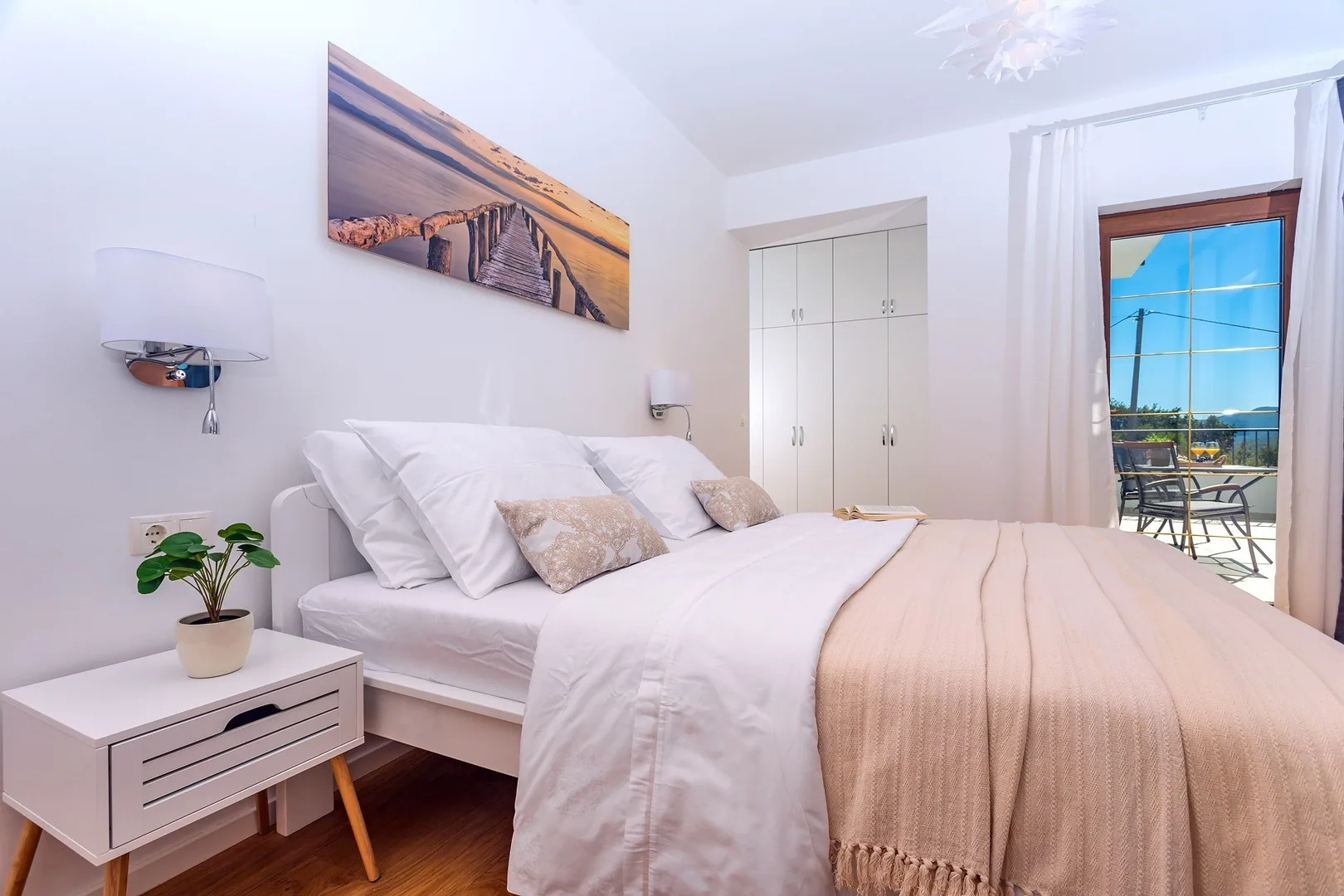 A bright bedroom with a neatly made bed and a window opening onto a balcony.