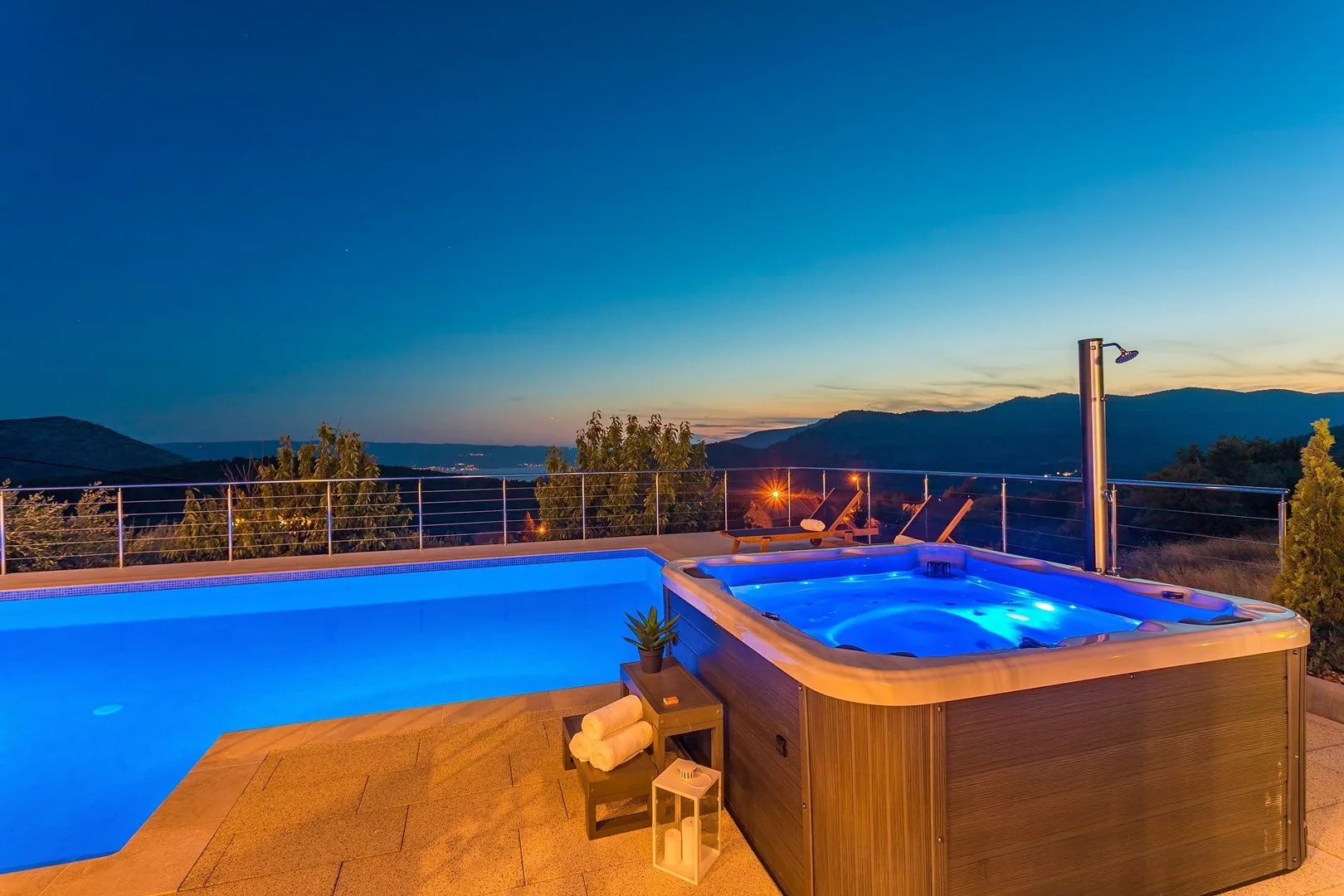 An outdoor pool and hot tub overlook distant mountains at dusk.