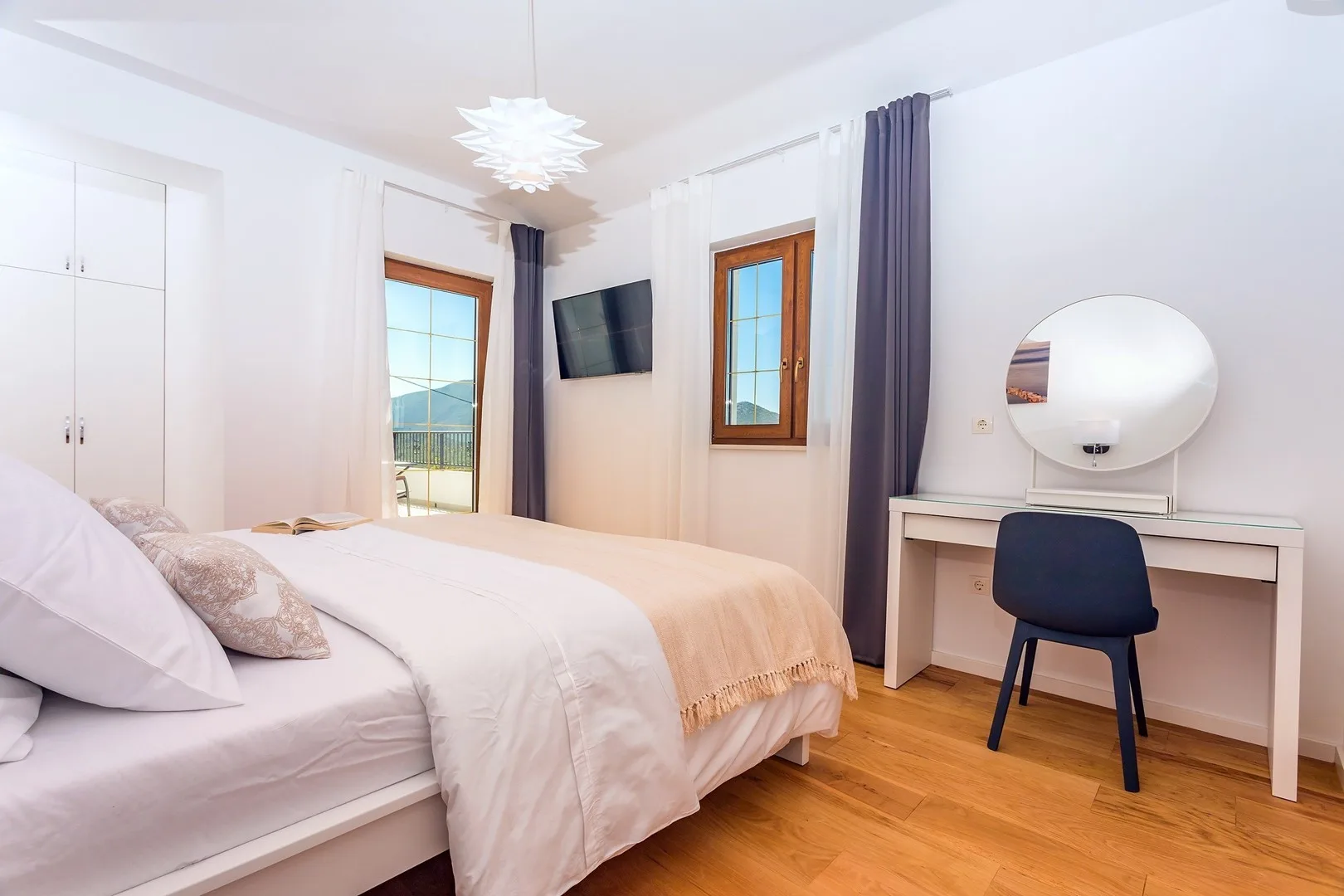 A bright bedroom with a bed, desk, and windows overlooking the outdoors.